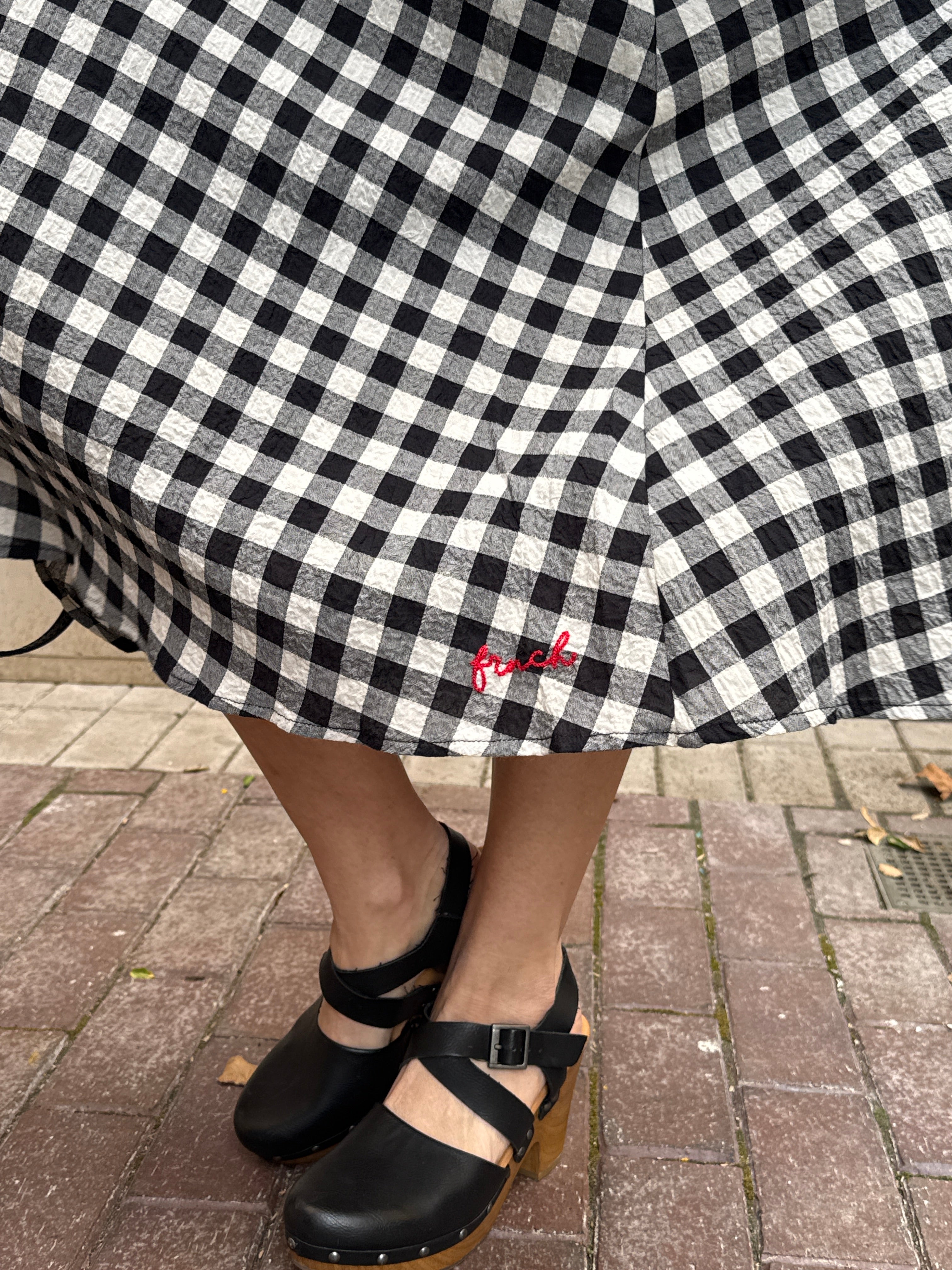 Person wearing a black and white checkered skirt with sandals on a sidewalk.
