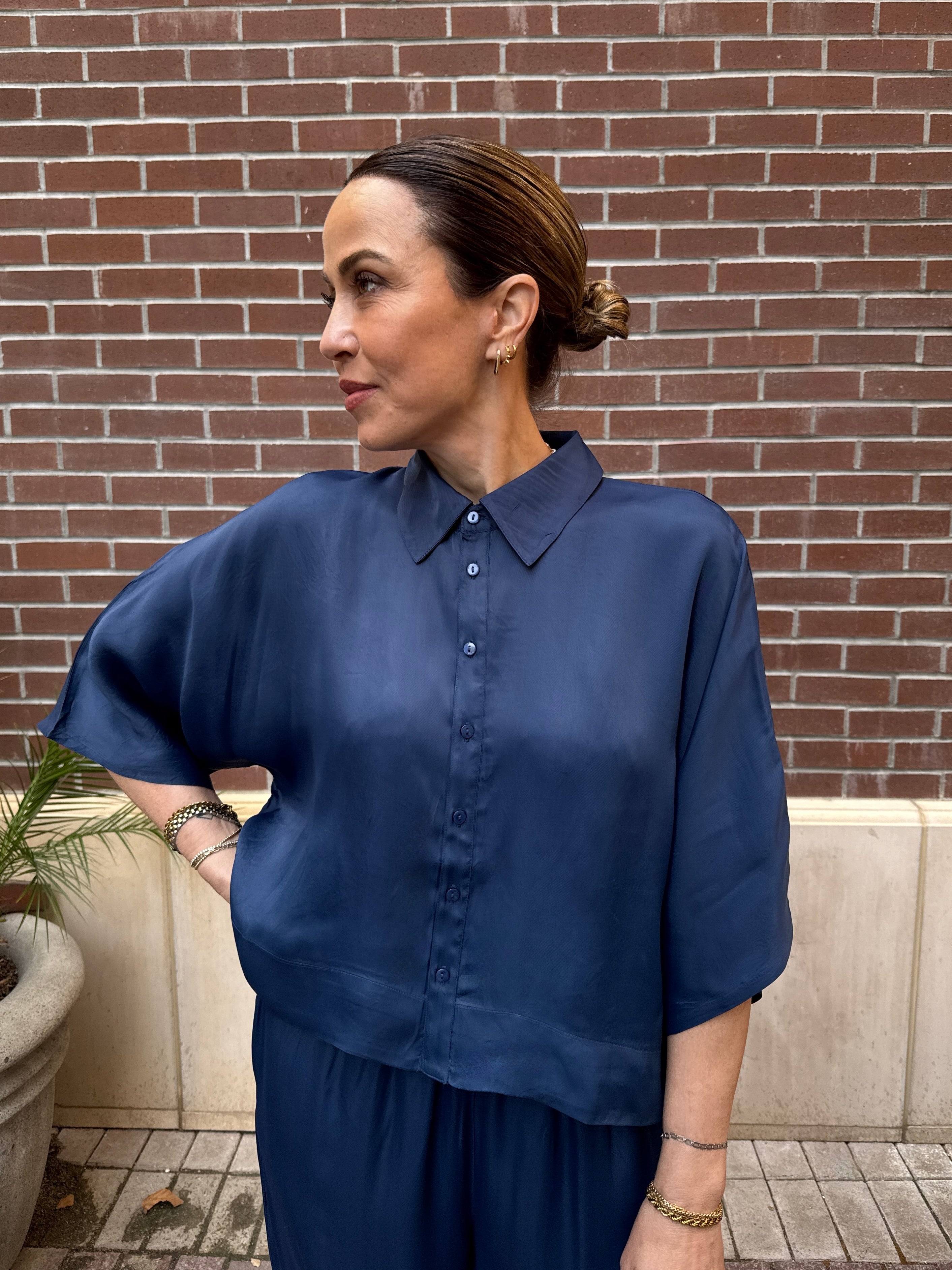 Woman wearing a blue shirt standing against a brick wall.