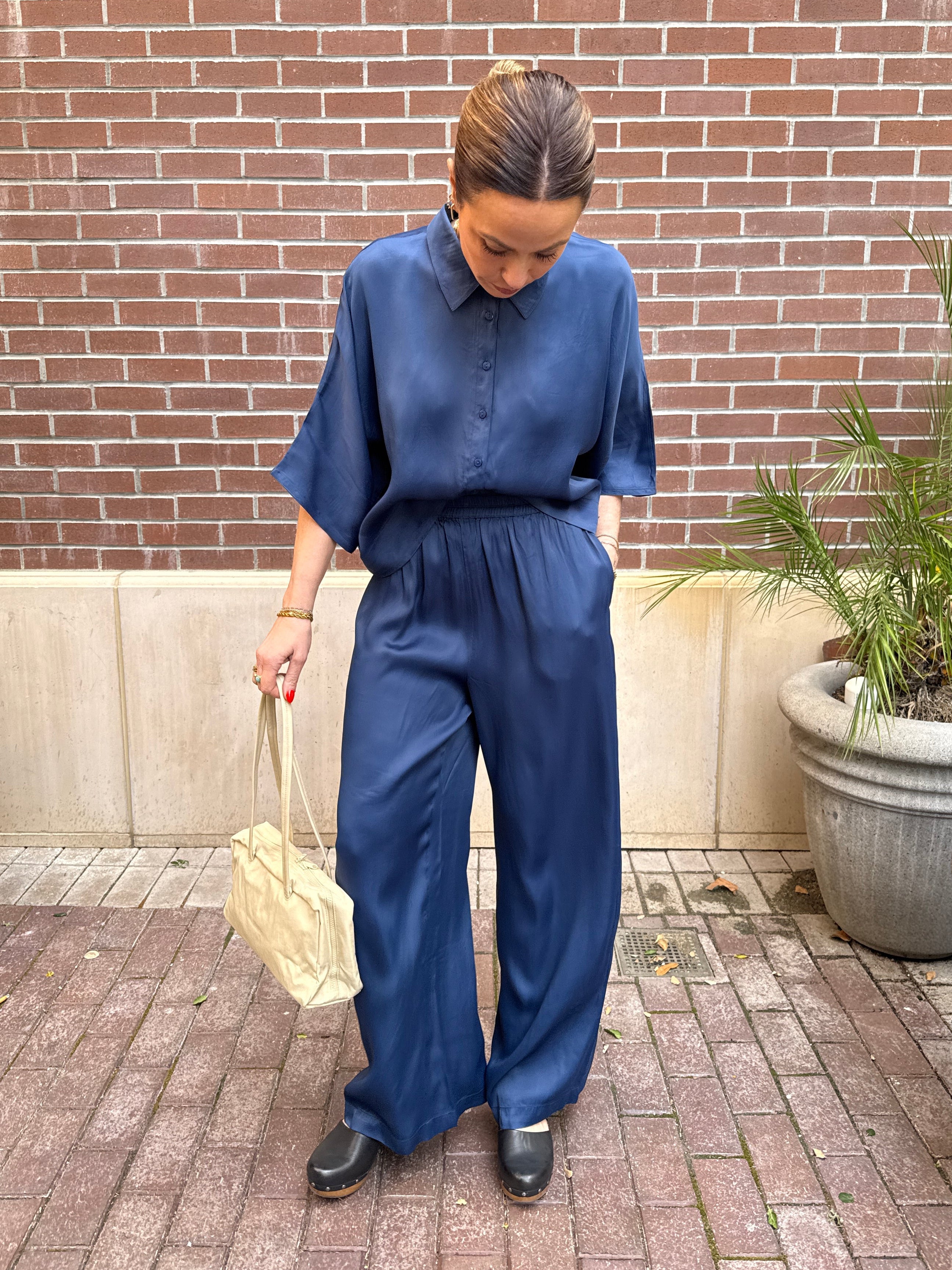 Person wearing a blue outfit standing on a brick patio with plants in the background