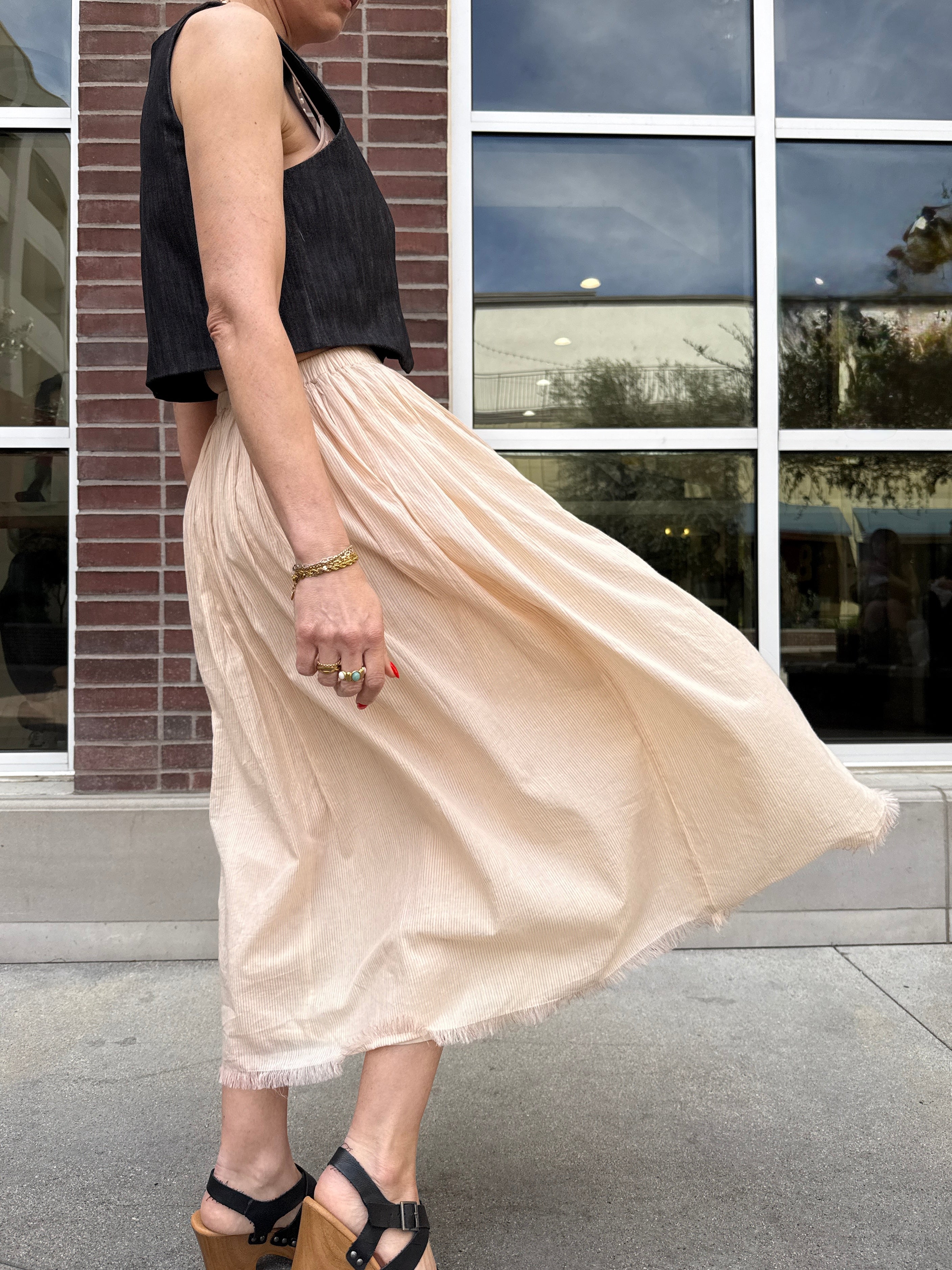 Person wearing a black top and beige skirt standing in front of a building with reflective windows.