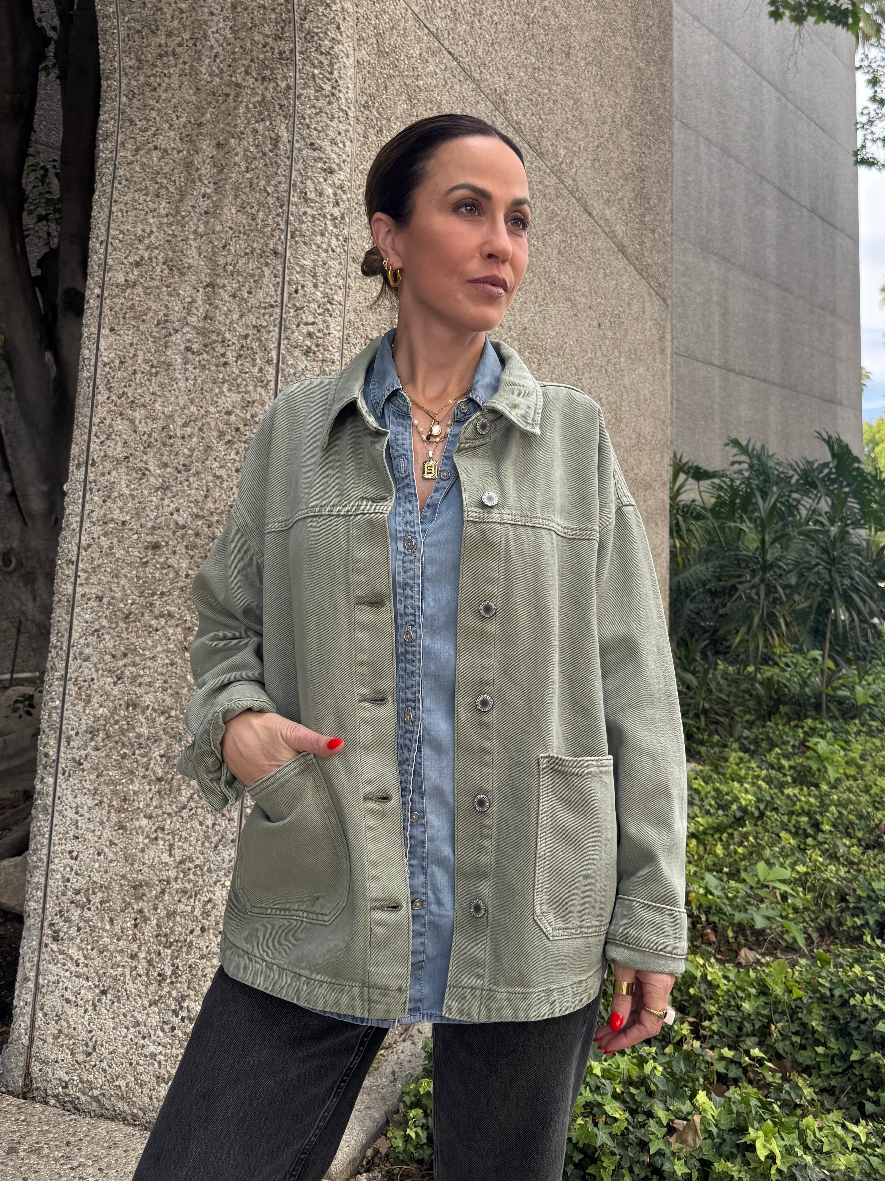 Woman wearing a green jacket over a denim shirt standing outdoors.