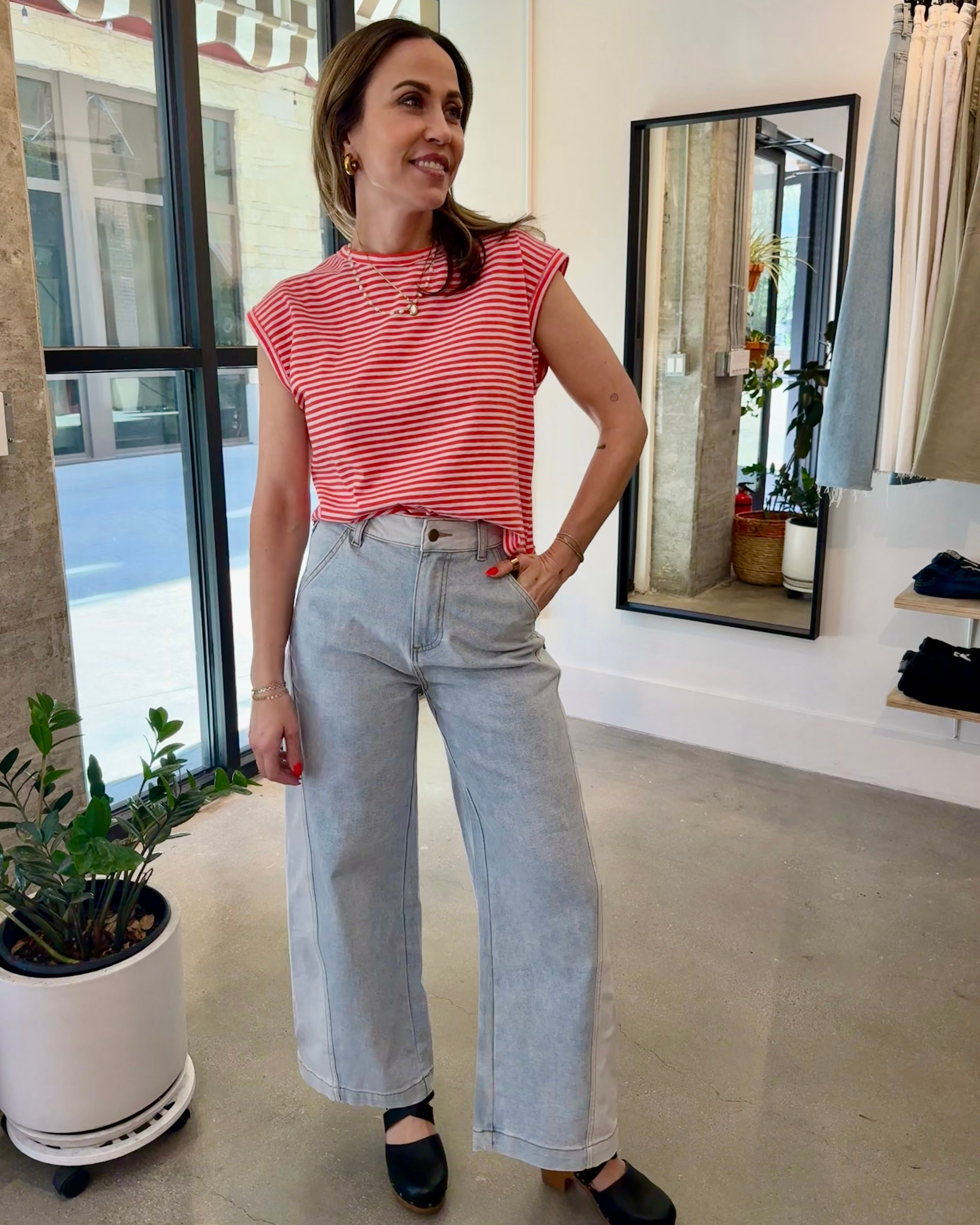 Woman in a red striped shirt and light blue jeans standing in a modern interior setting.
