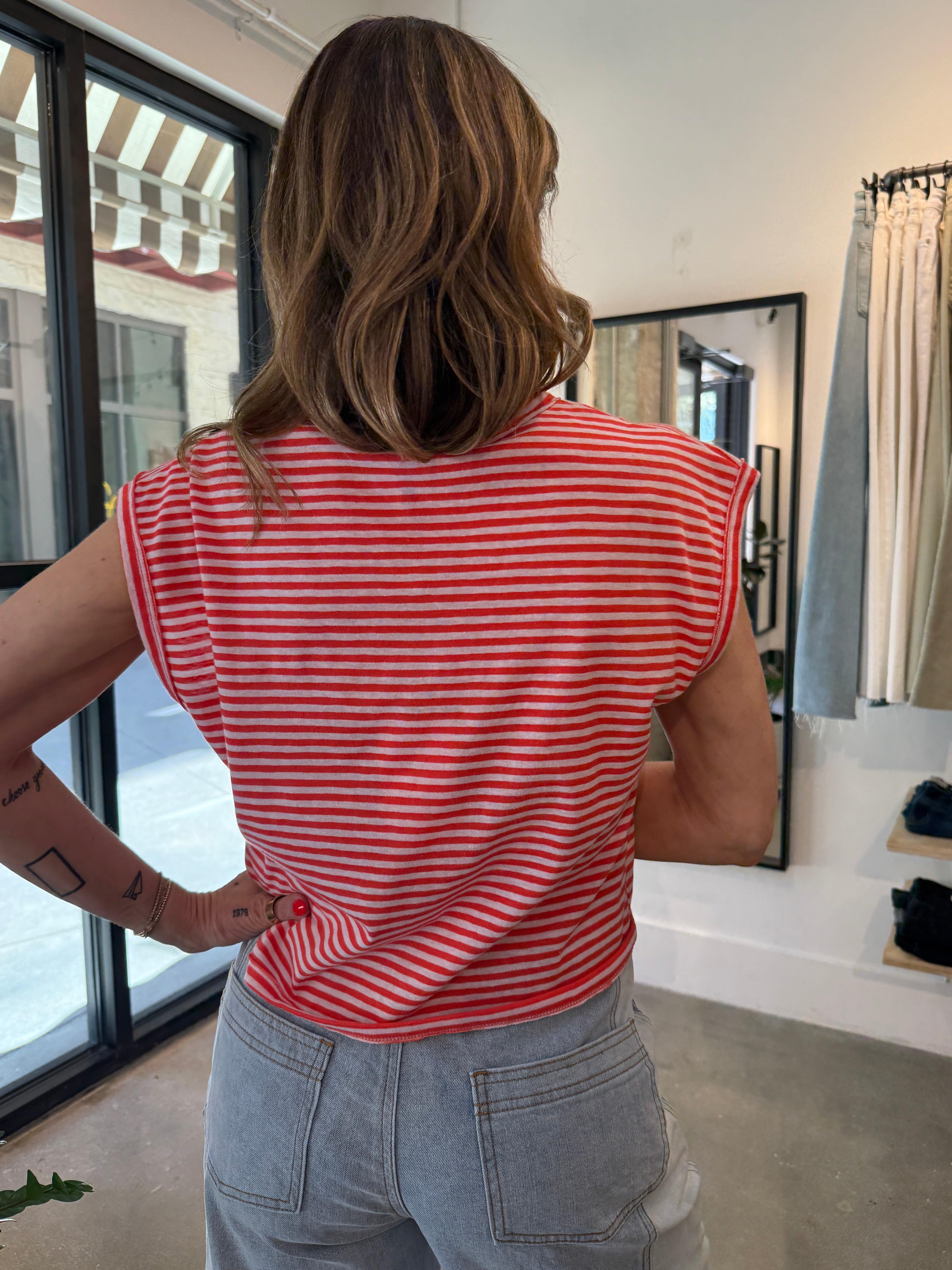 Person wearing a red and white striped sleeveless top and light blue jeans in an indoor setting.