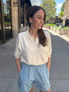 woman outside wearing a cream short sleeve sweater with blue shorts. 