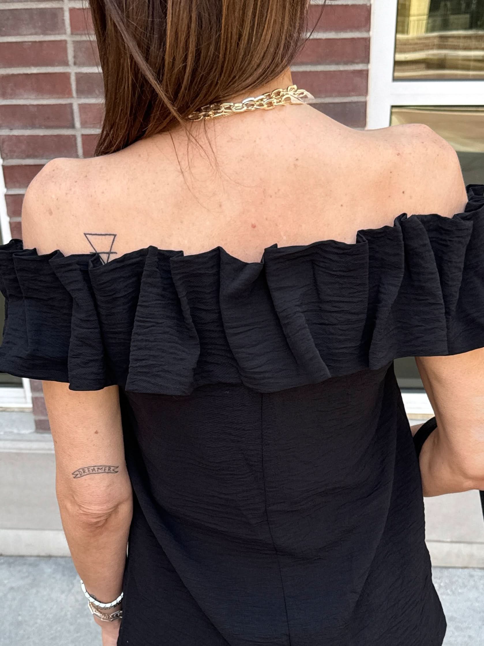 Woman with her back turned wearing a black off the shoulder ruffle top. 