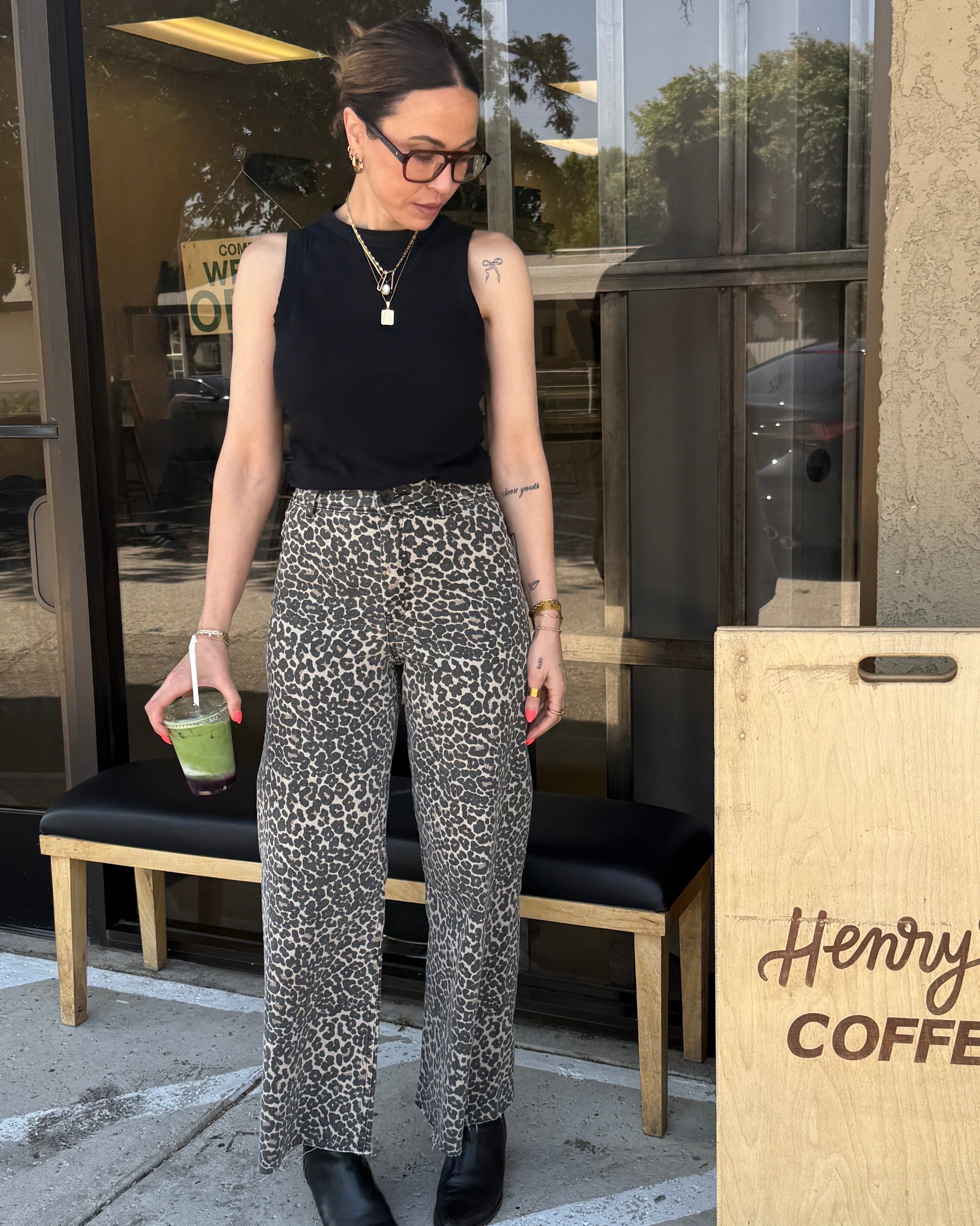 Woman in leopard print pants and black top standing outside a coffee shop.