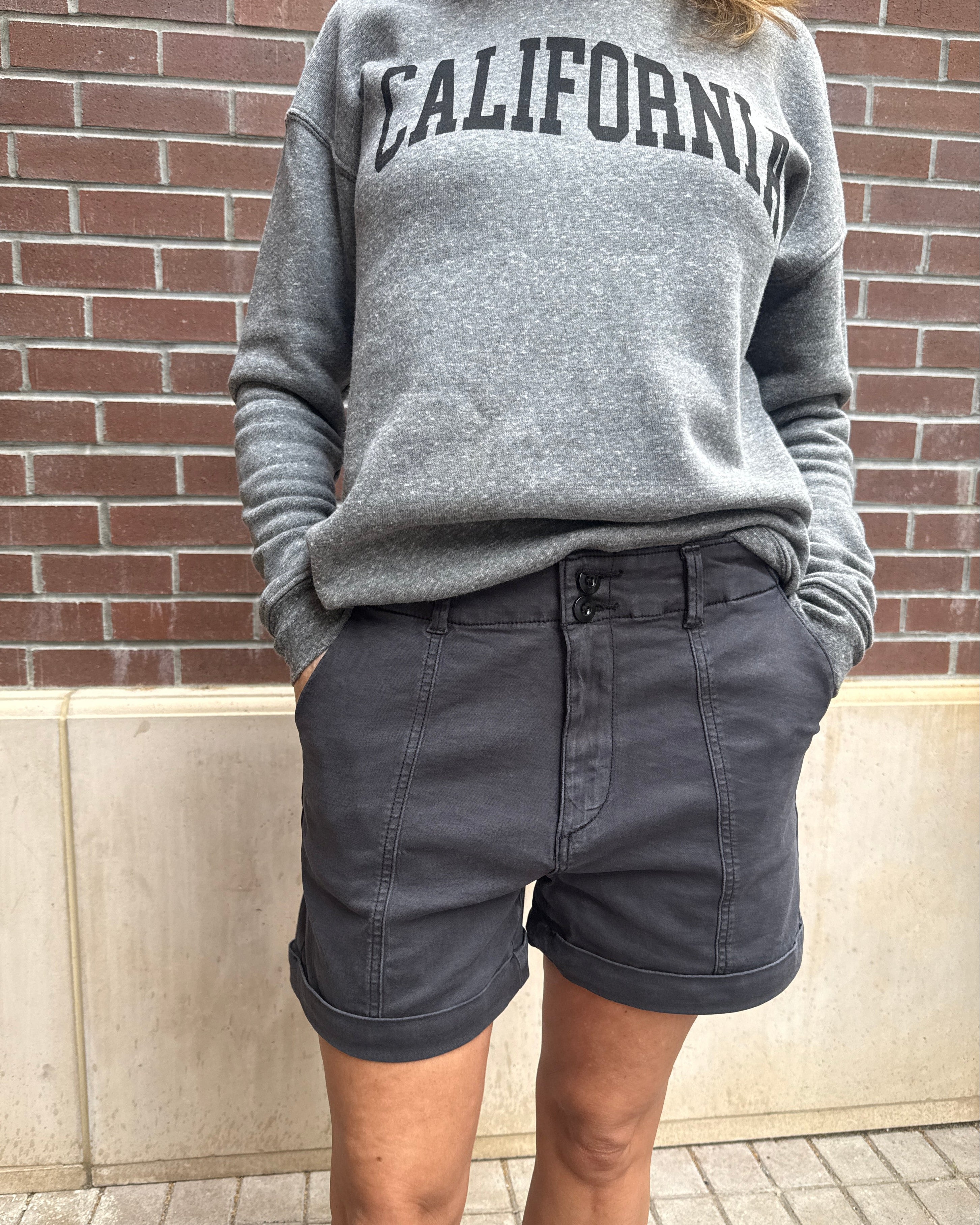 Person wearing a gray hoodie with 'California' text and dark shorts on a sidewalk.