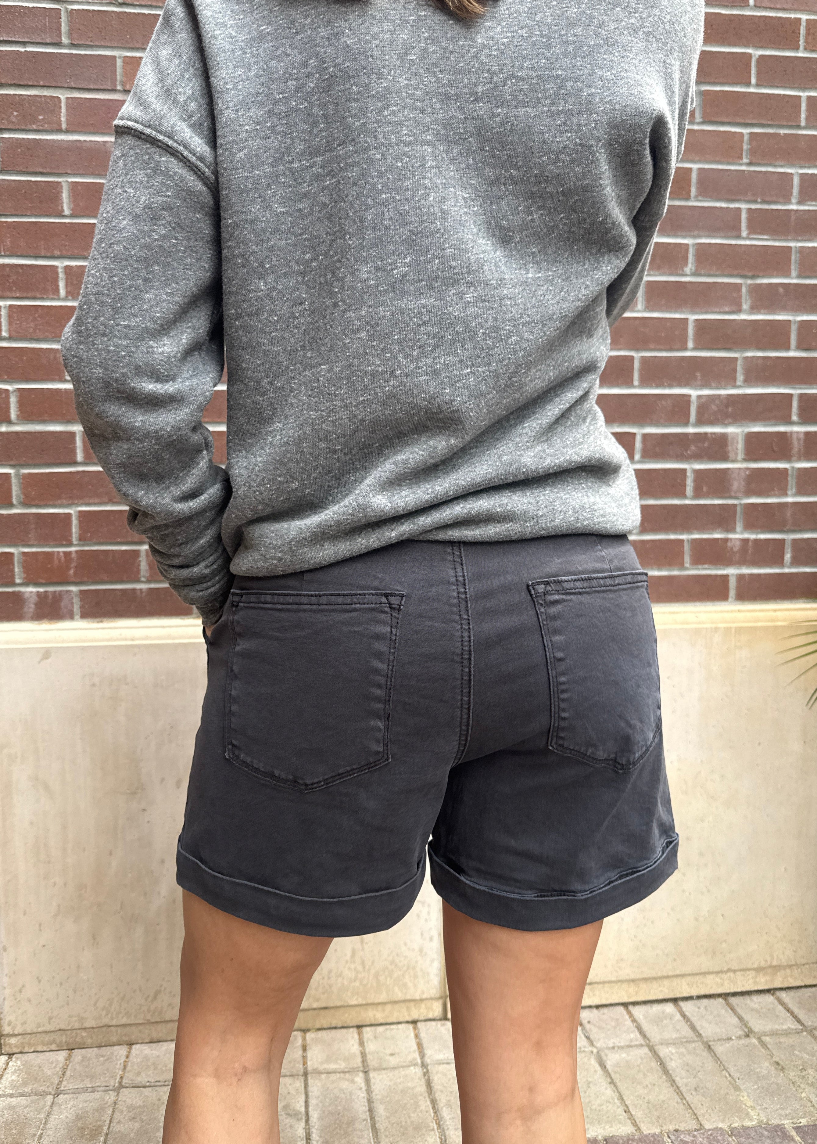 Person wearing a gray sweatshirt and black shorts on a tiled floor.