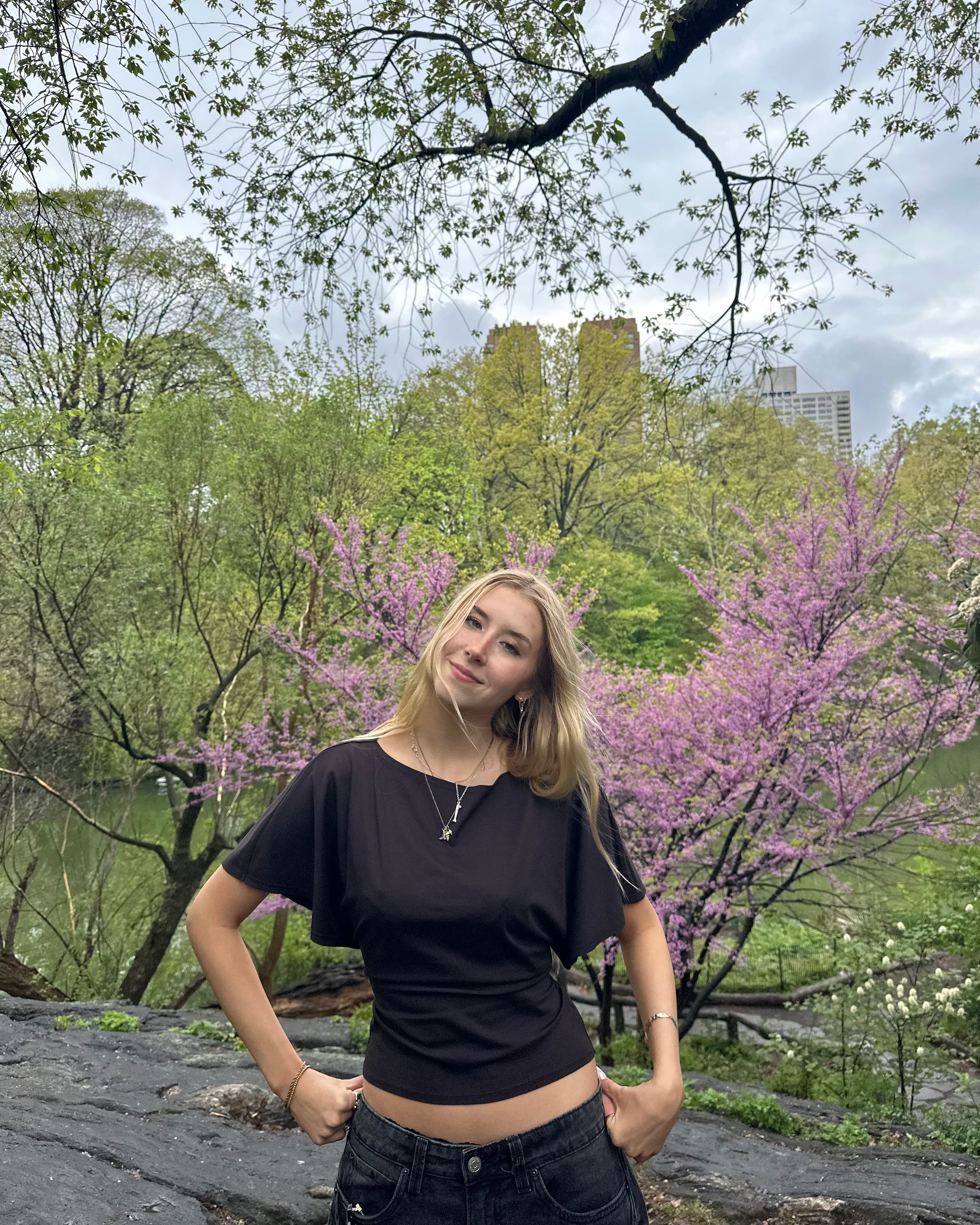 Person standing in a park with blooming trees and a cloudy sky
