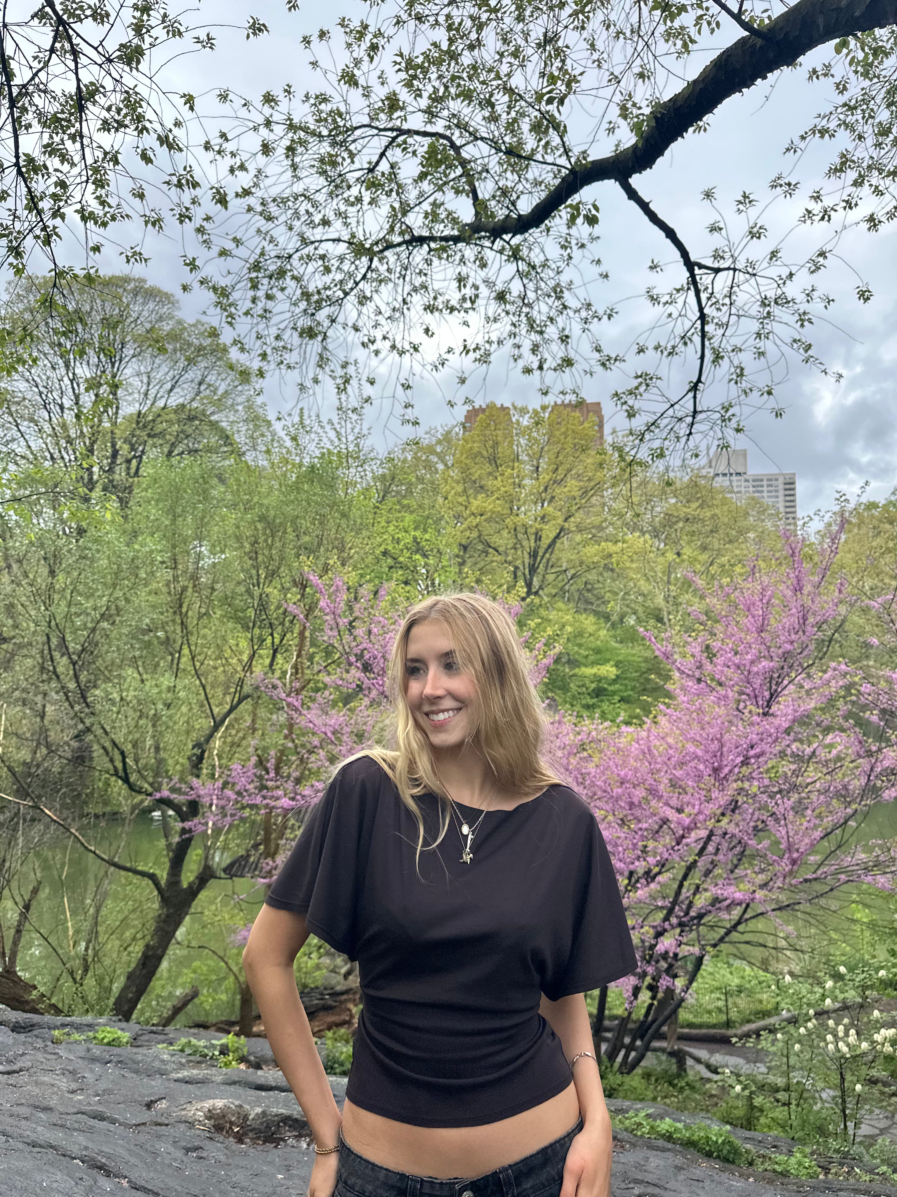 Woman standing in a park with trees and pink flowers in the background