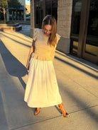 woman walking outside wearing white dress with brown knit top brown boots 