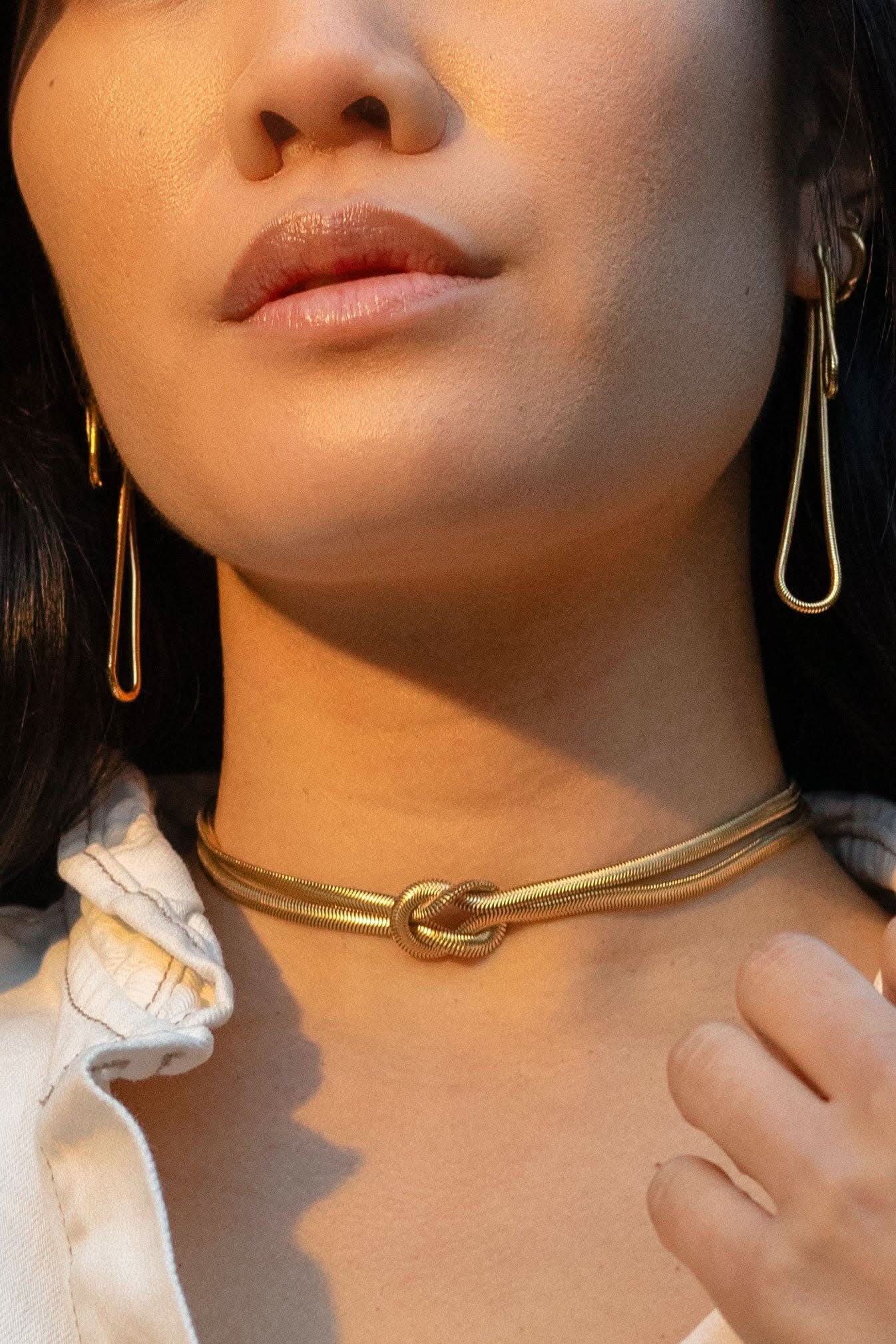 Woman wearing long abstract loop earrings and gold figure eight knot herringbone choker necklace 