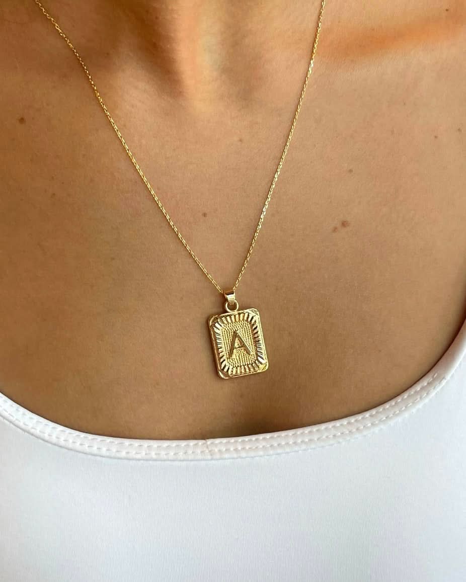 Woman wearing a letter A tarnish free gold initial charm necklace while wearing a white tank top. 