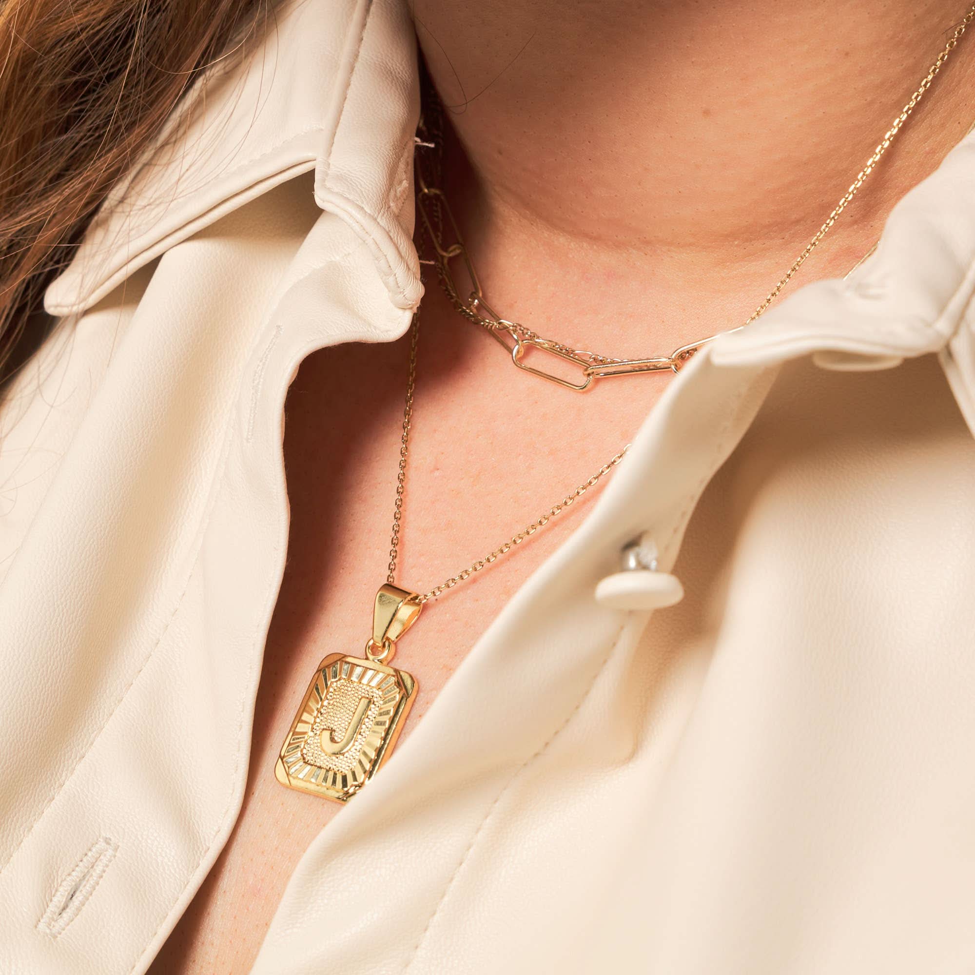 Woman wearing a letter J tarnish free gold initial charm necklace with a gold chain necklace. 