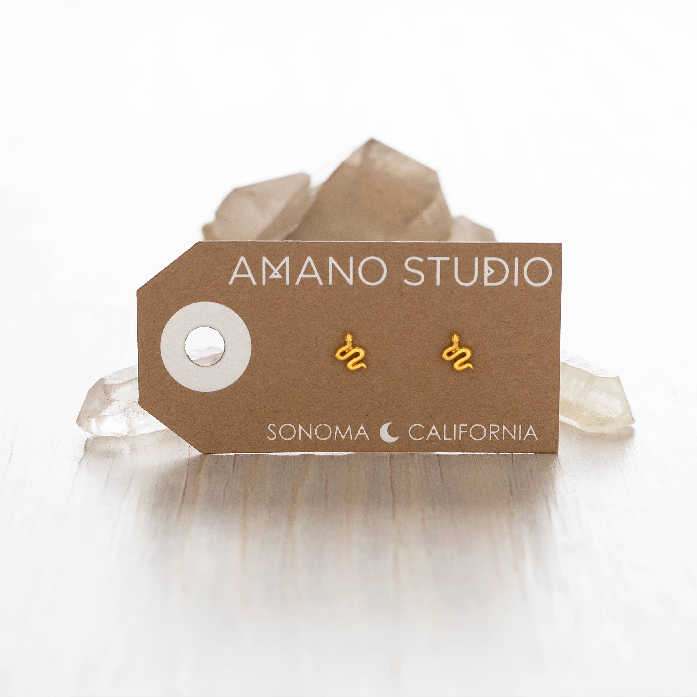 Gold earrings on a 'Amano Studio' branded card with a brow card