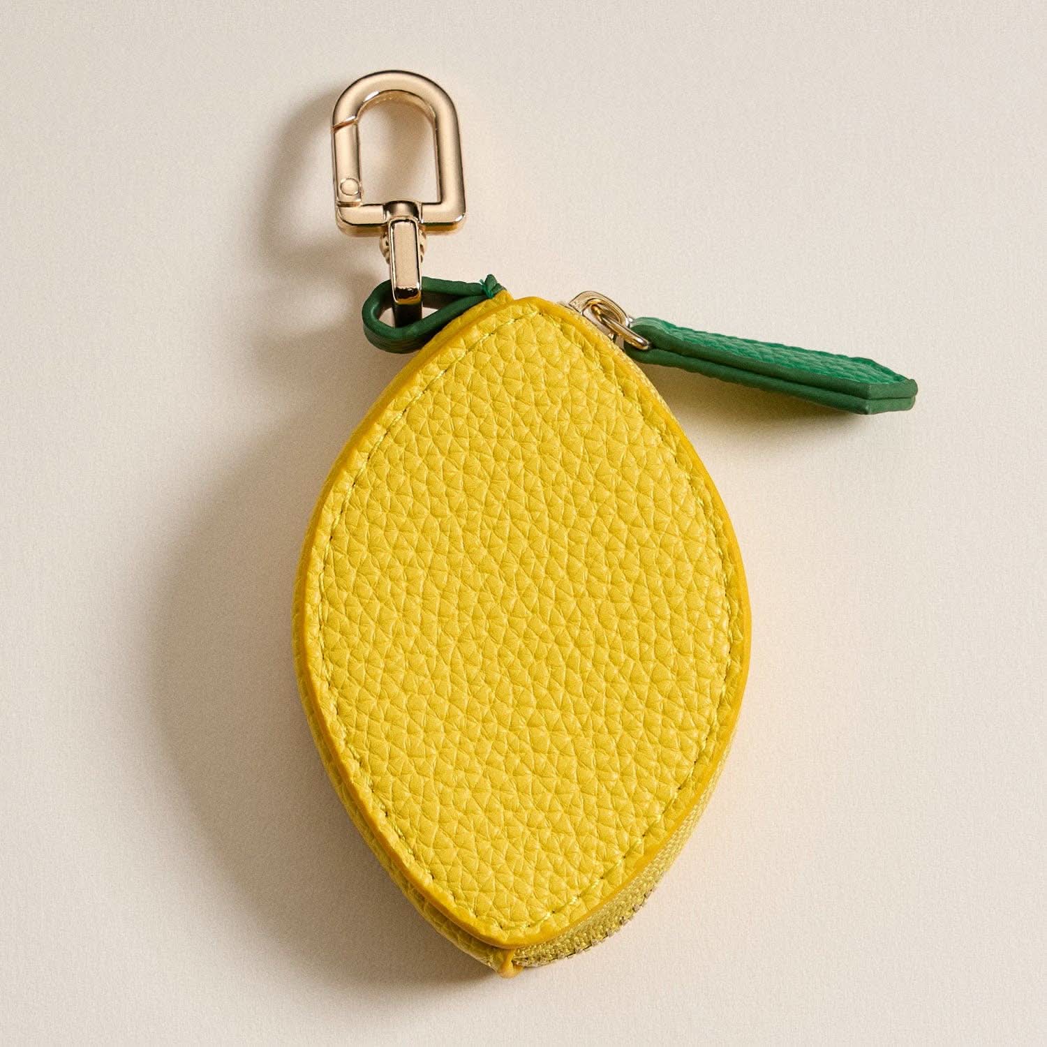 Yellow lemon-shaped keychain with a green strap on a beige background