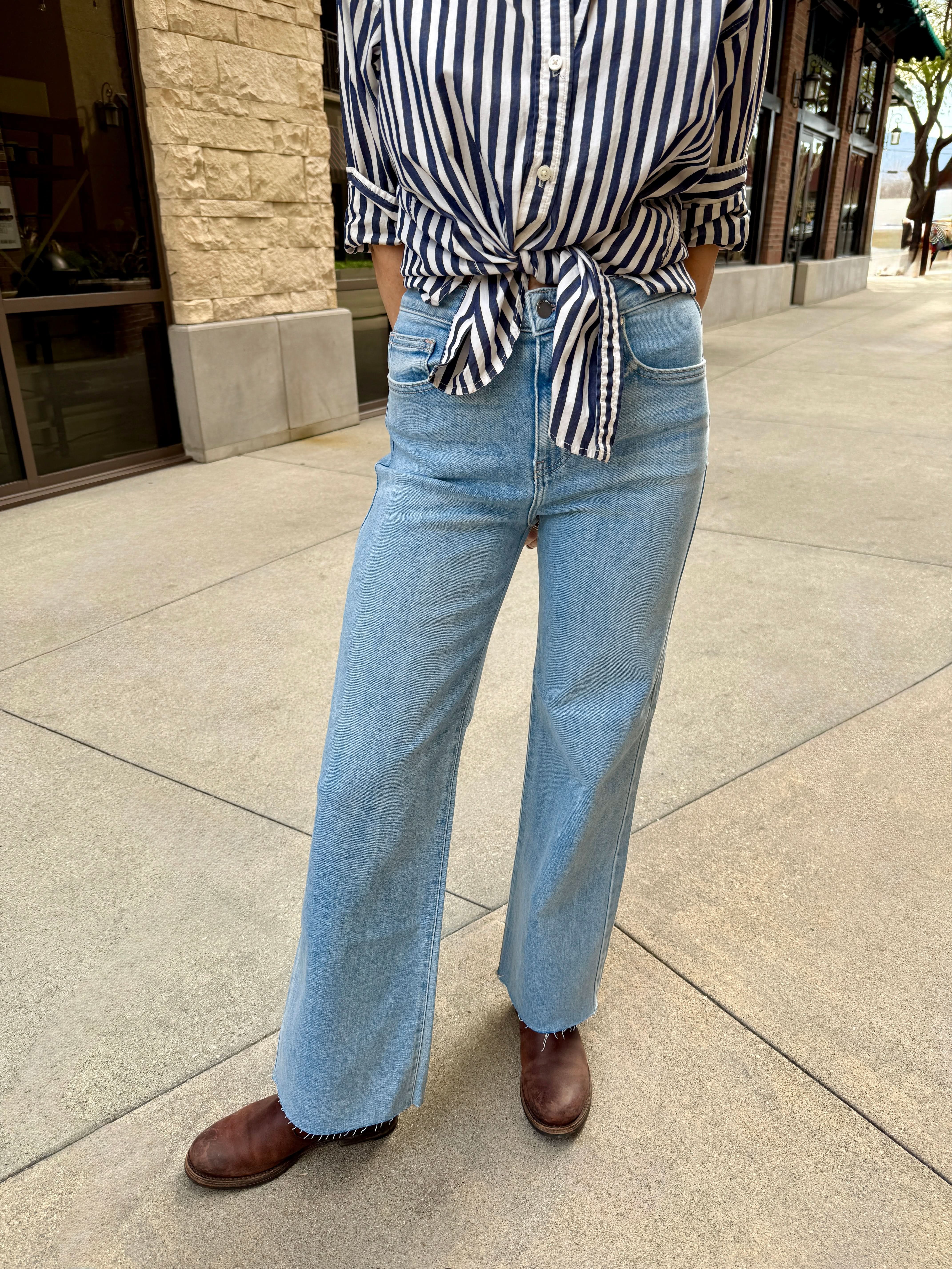Woman standing outside wearing light wash raw hem jeans with navy blue 