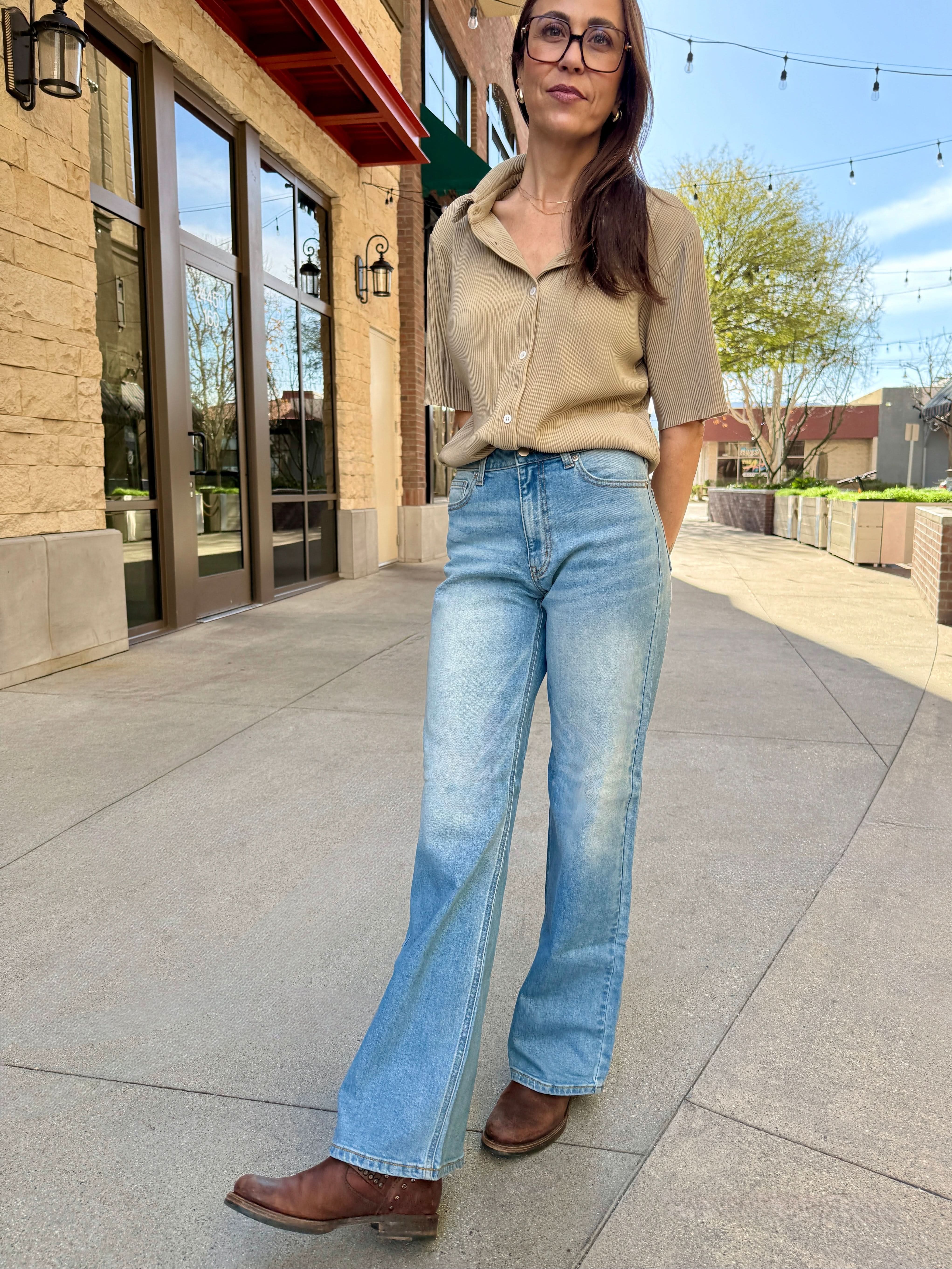 Woman wearing a beige top and blue jeans standing on a sidewalk.