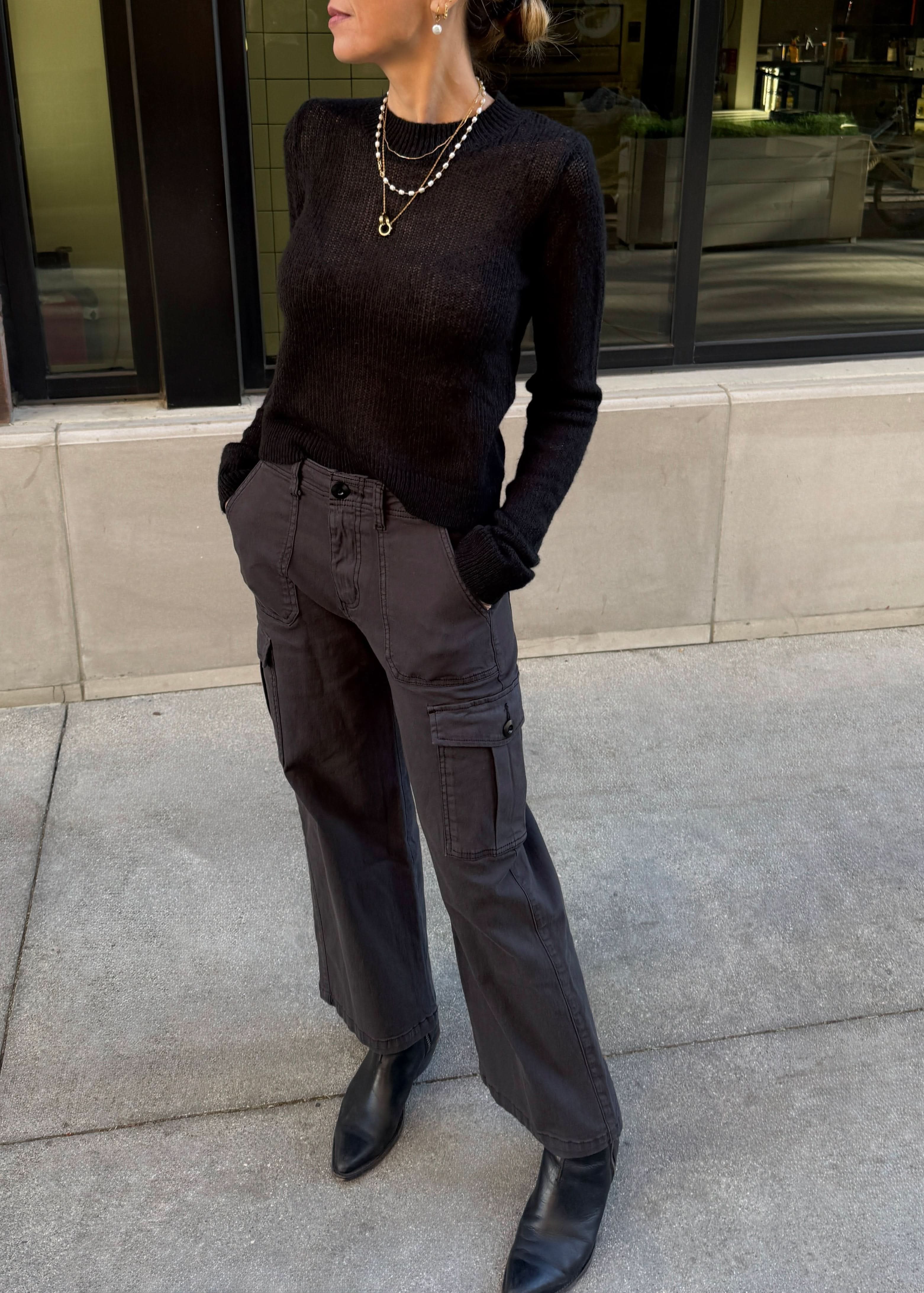 Person wearing a black sweater and gray cargo pants standing on a sidewalk.