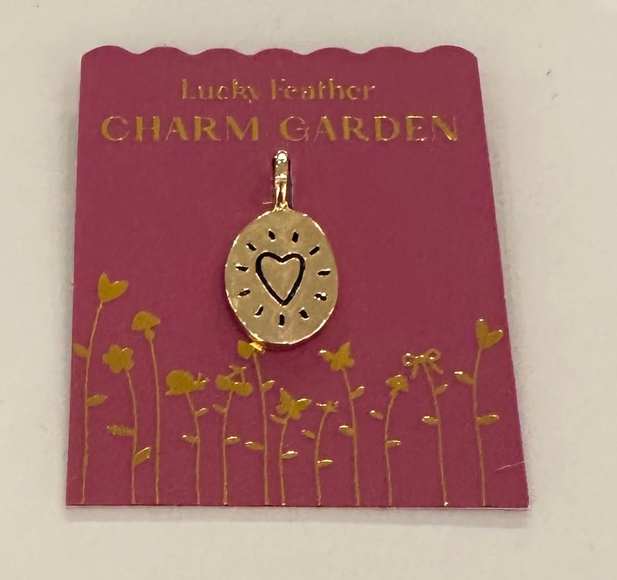 Gold charm with heart design on a 'Lucky Feather Charm Garden' card
