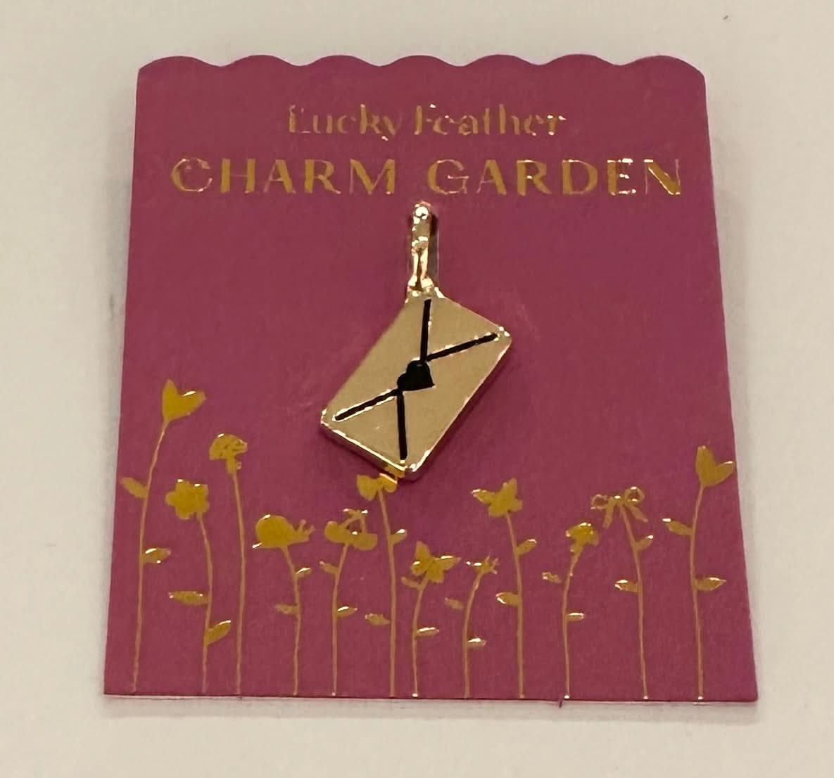 Gold charm on a 'Lucky Feather Charm Garden' card with floral design