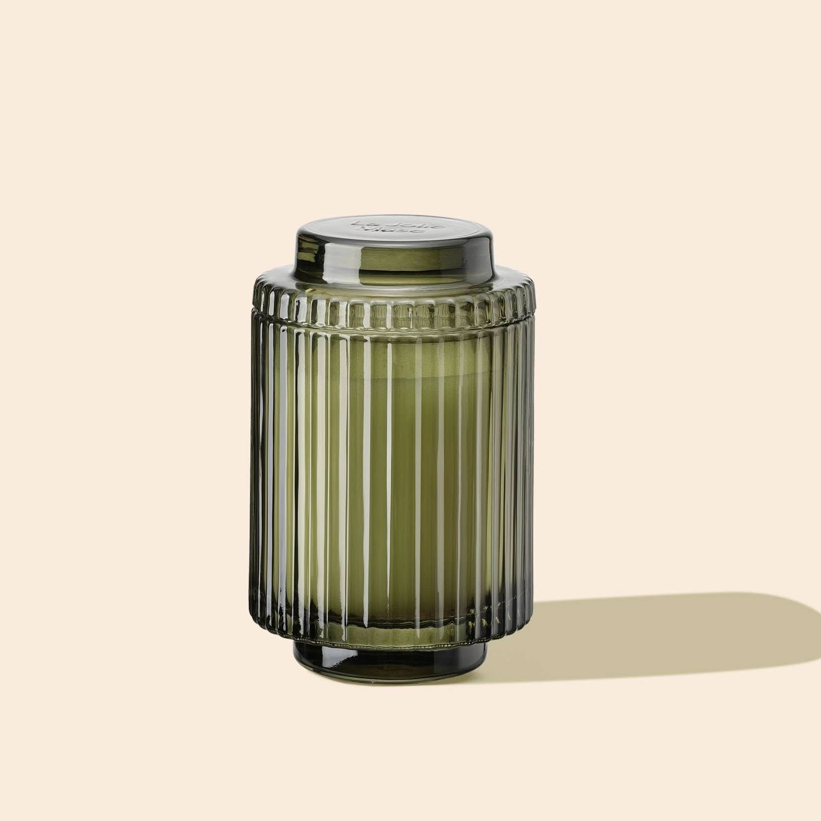 Green ribbed glass jar with a lid on a beige background