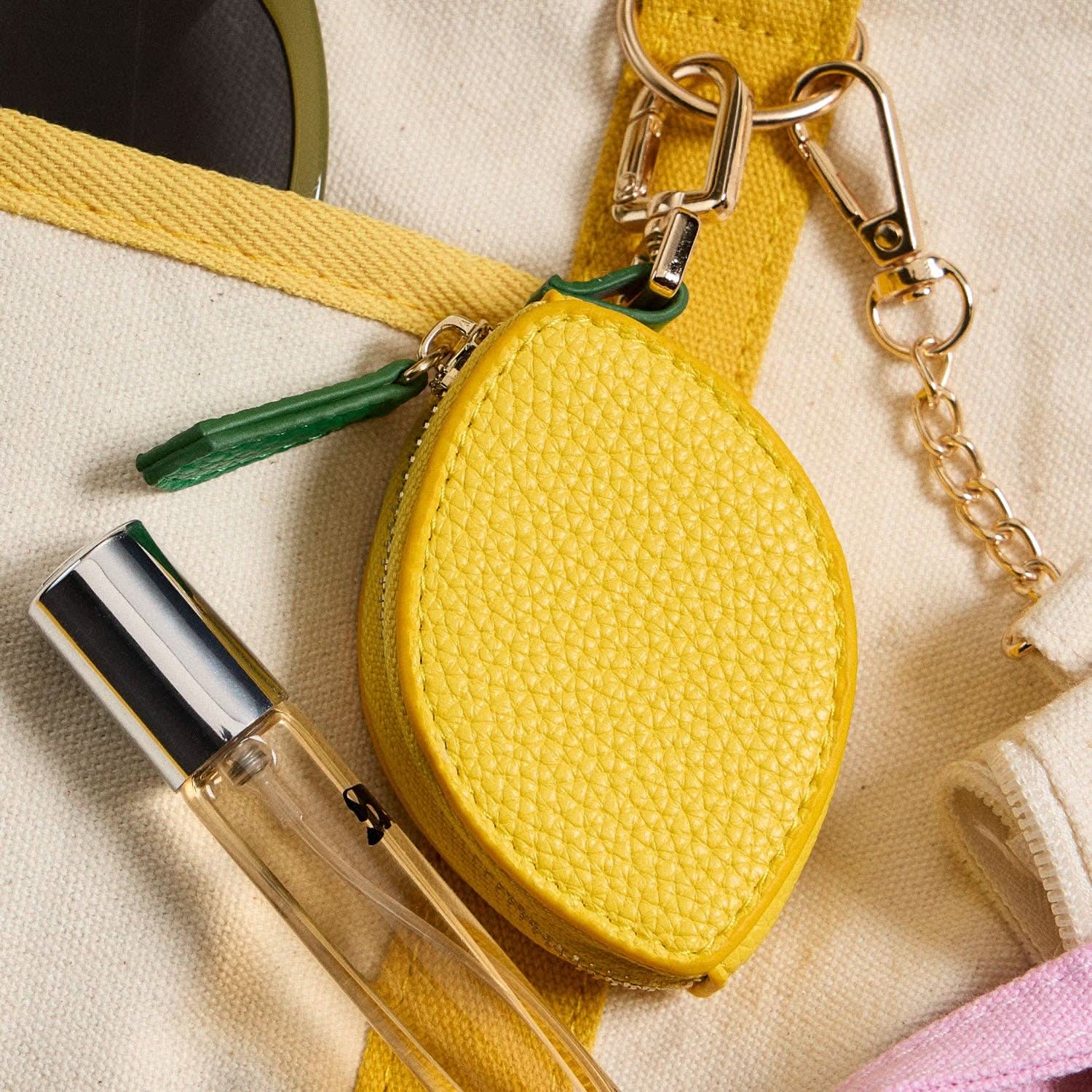 Yellow lemon-shaped pouch with a keychain on a beige background