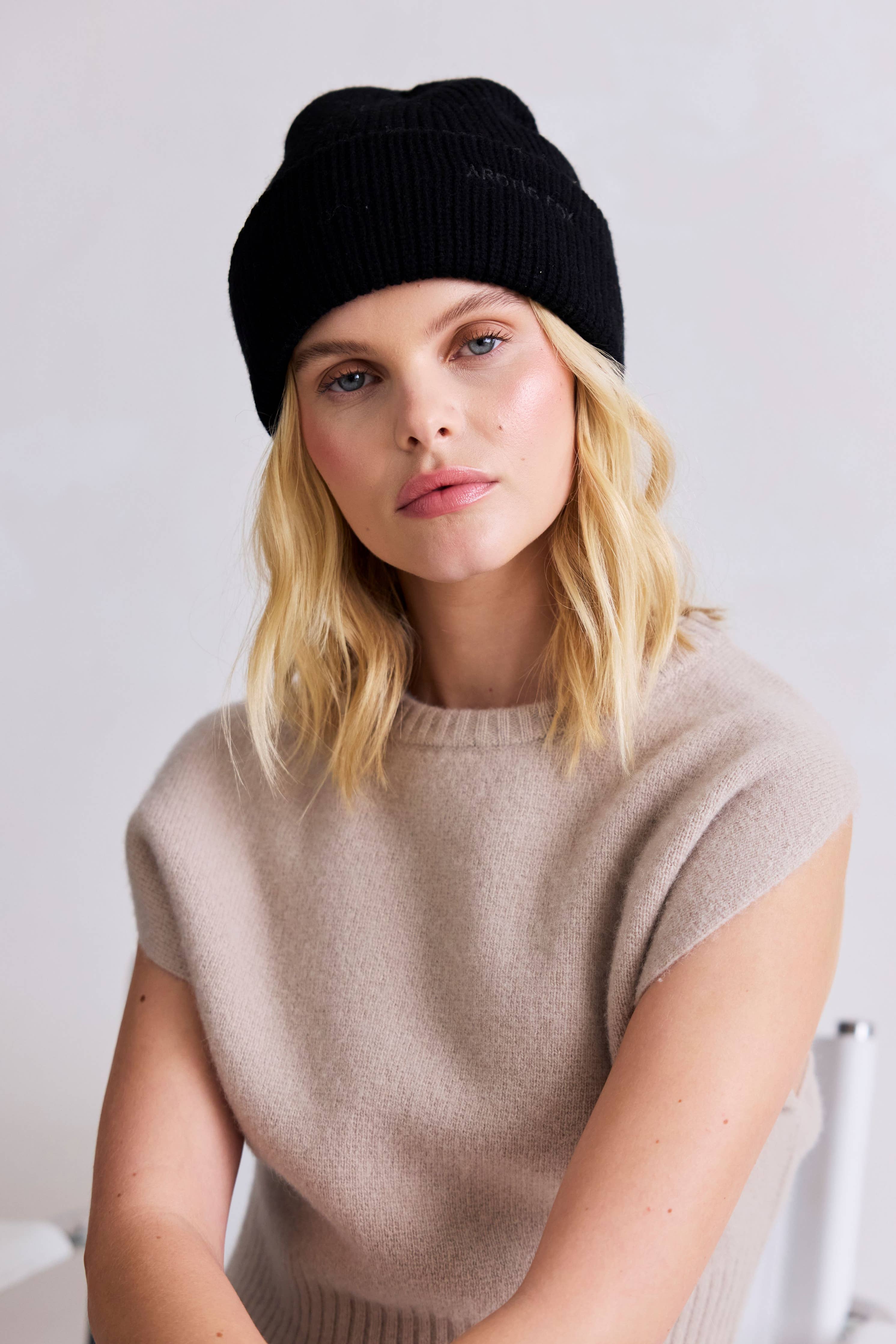 Woman wearing a black beanie and beige sweater against a white background