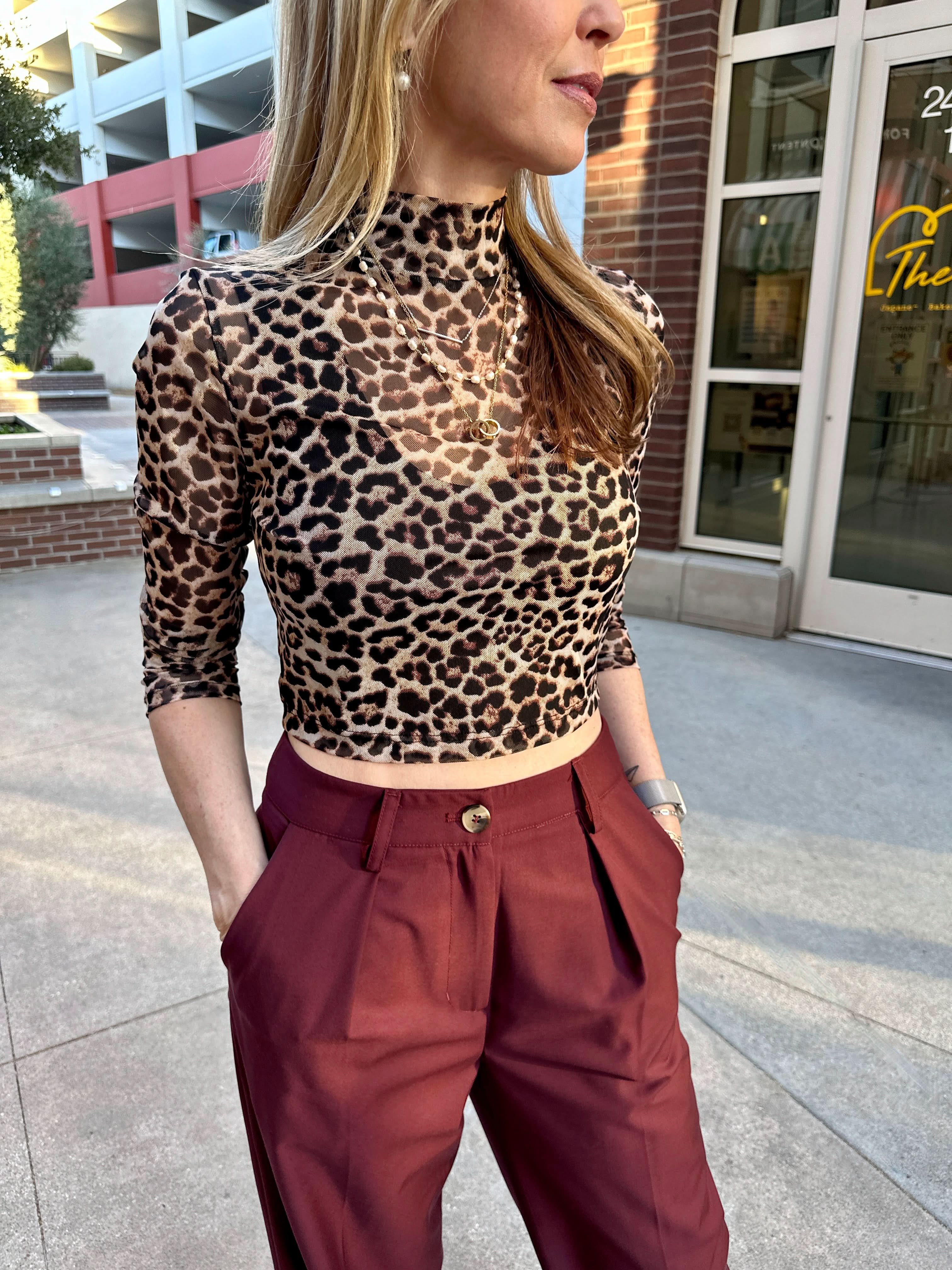 Person wearing a leopard print top and red pants standing outdoors.