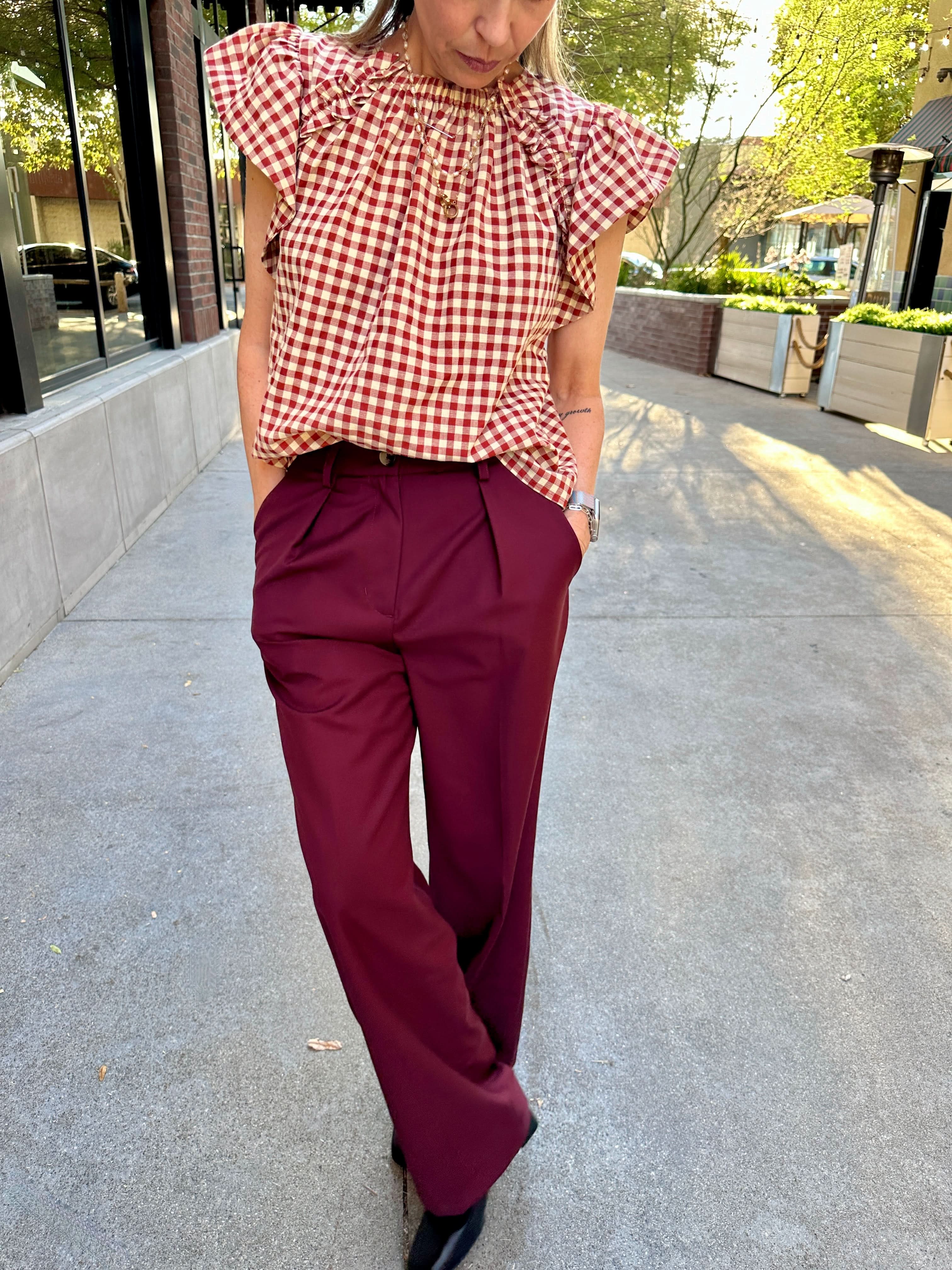 Person wearing a red and white checkered top and maroon pants on a sidewalk.