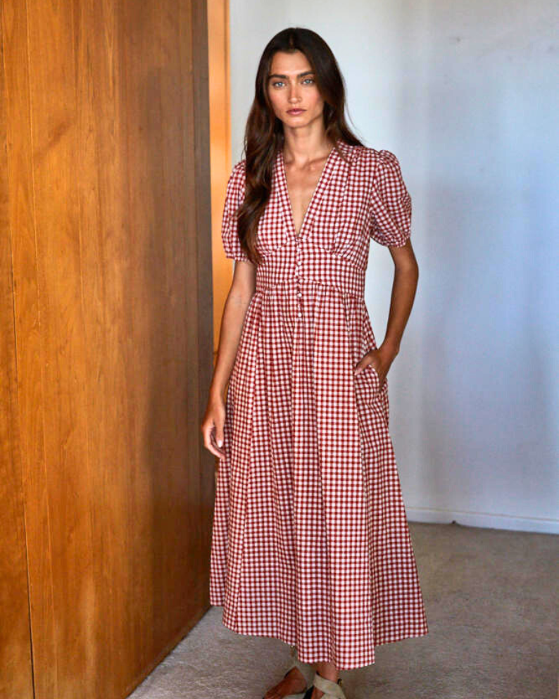 Woman wearing a red and white checkered dress standing against a wooden wall.
