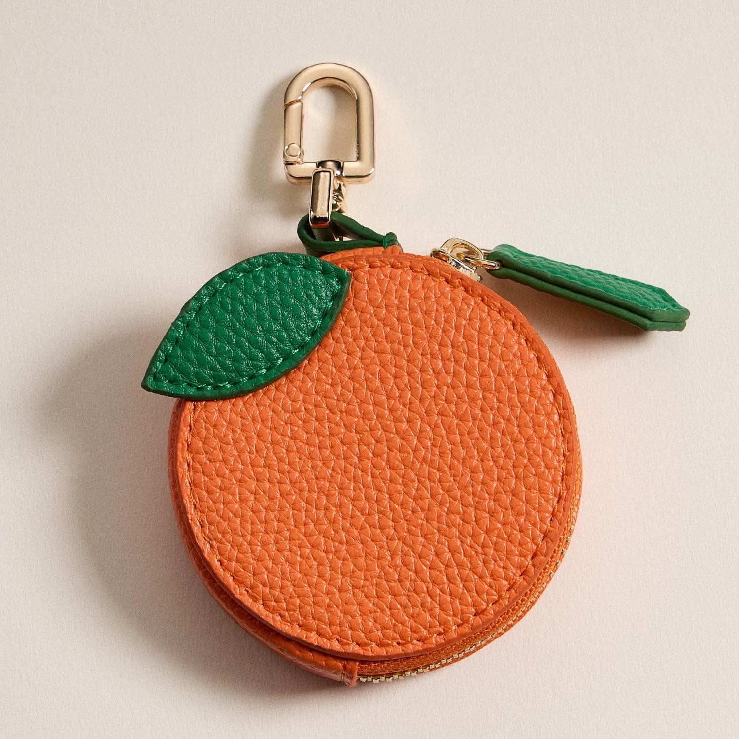 Orange-shaped keychain with green leaf on a beige background