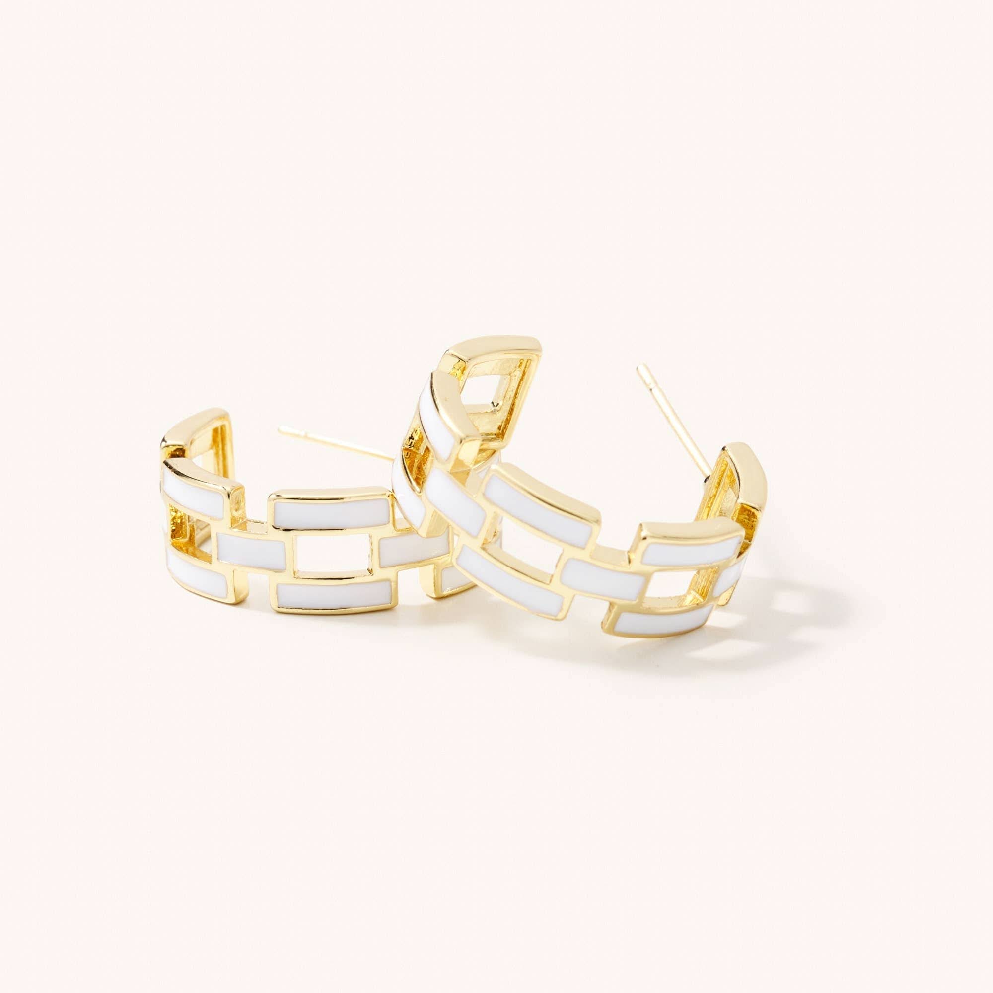 Gold hoop earrings with white geometric design on a light beige background