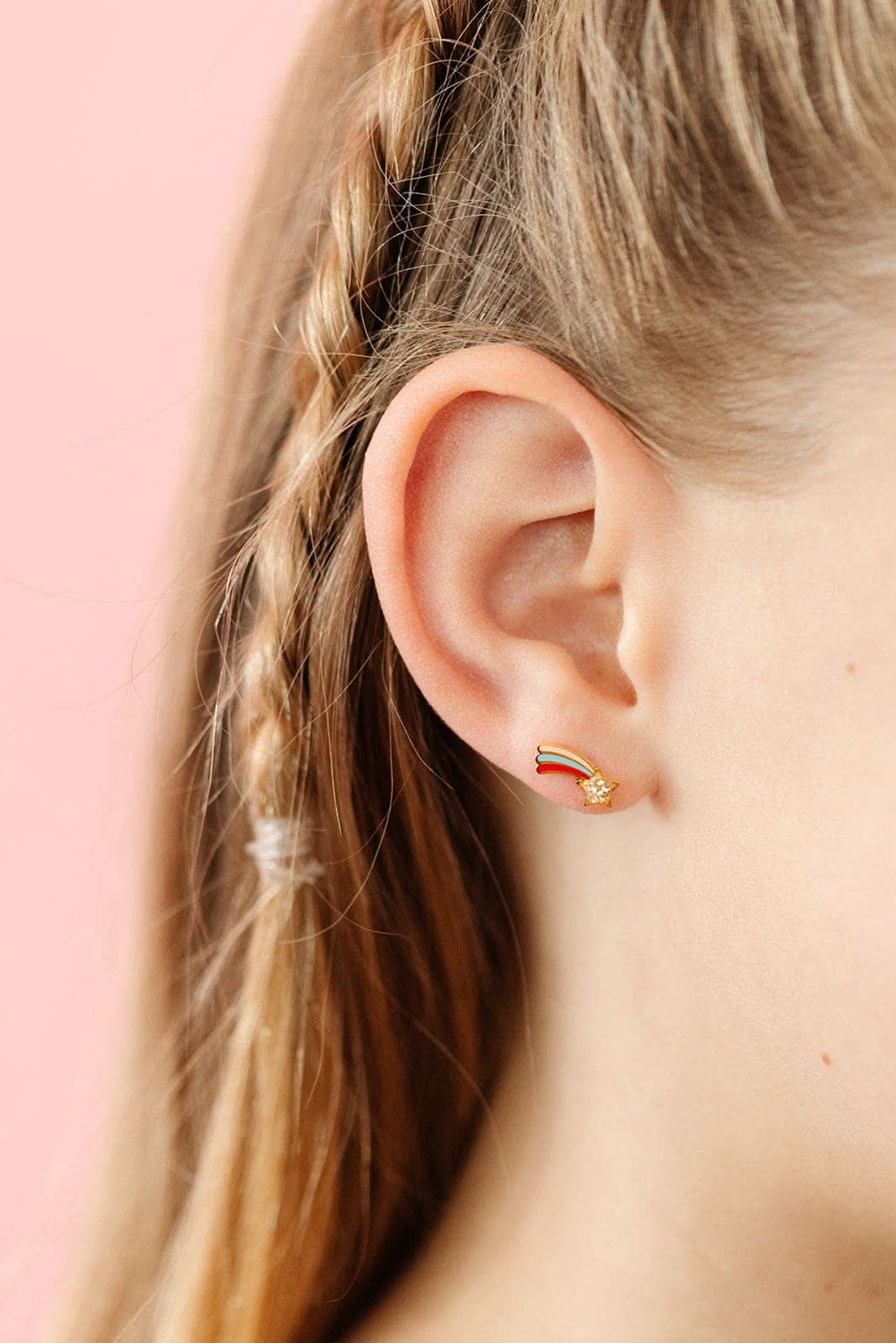 Close-up of an ear wearing a gold earring with a colorful design against a pink background