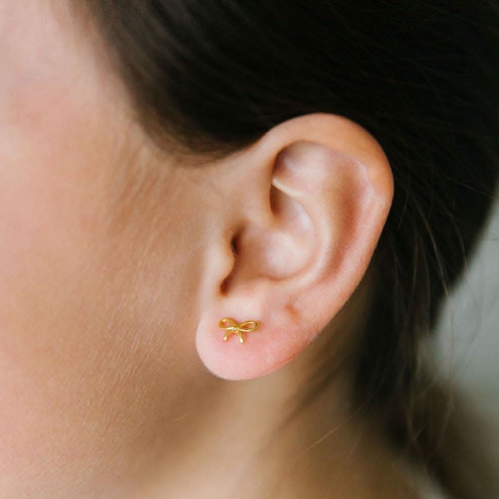 Gold bow-shaped earring on a person's weaing in ear