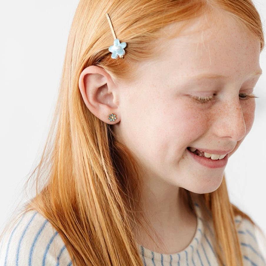 Close-up of a young girl with red hair wearing a floral hair clip and earrings on a white background