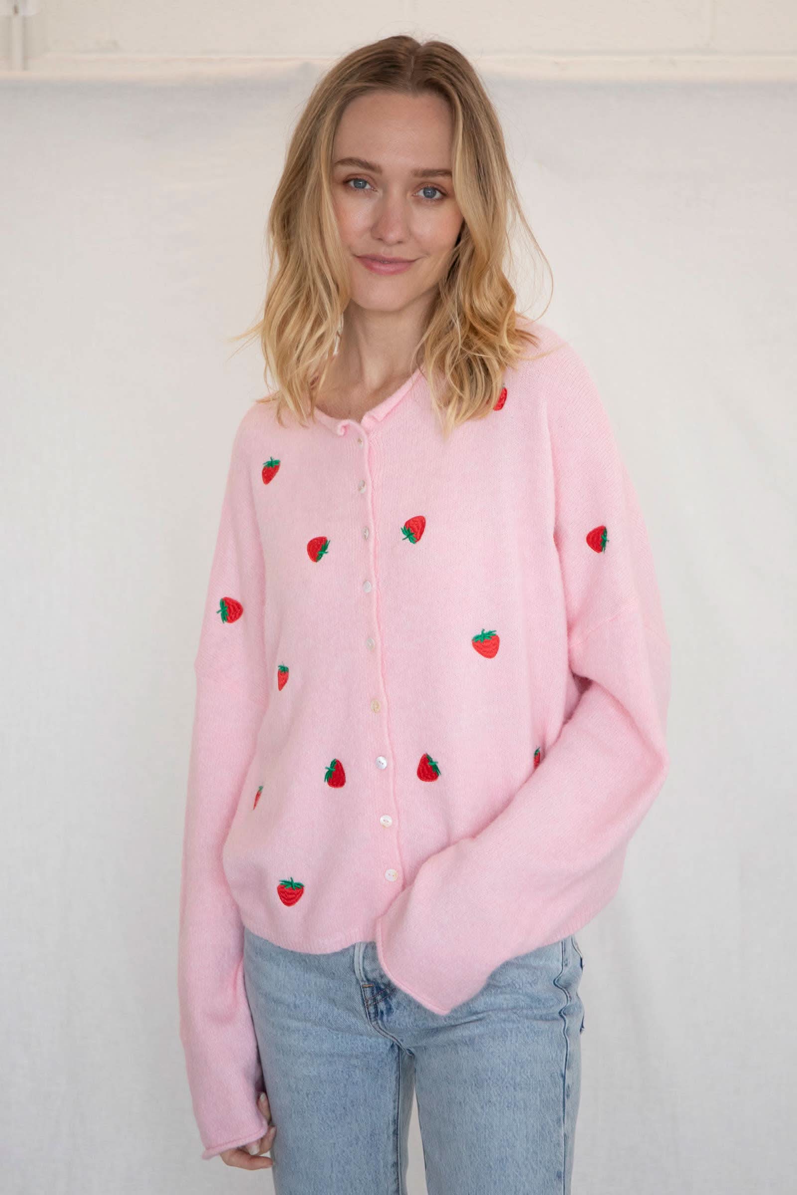 Woman wearing a pink button down cardigan with strawberries and blue jeans