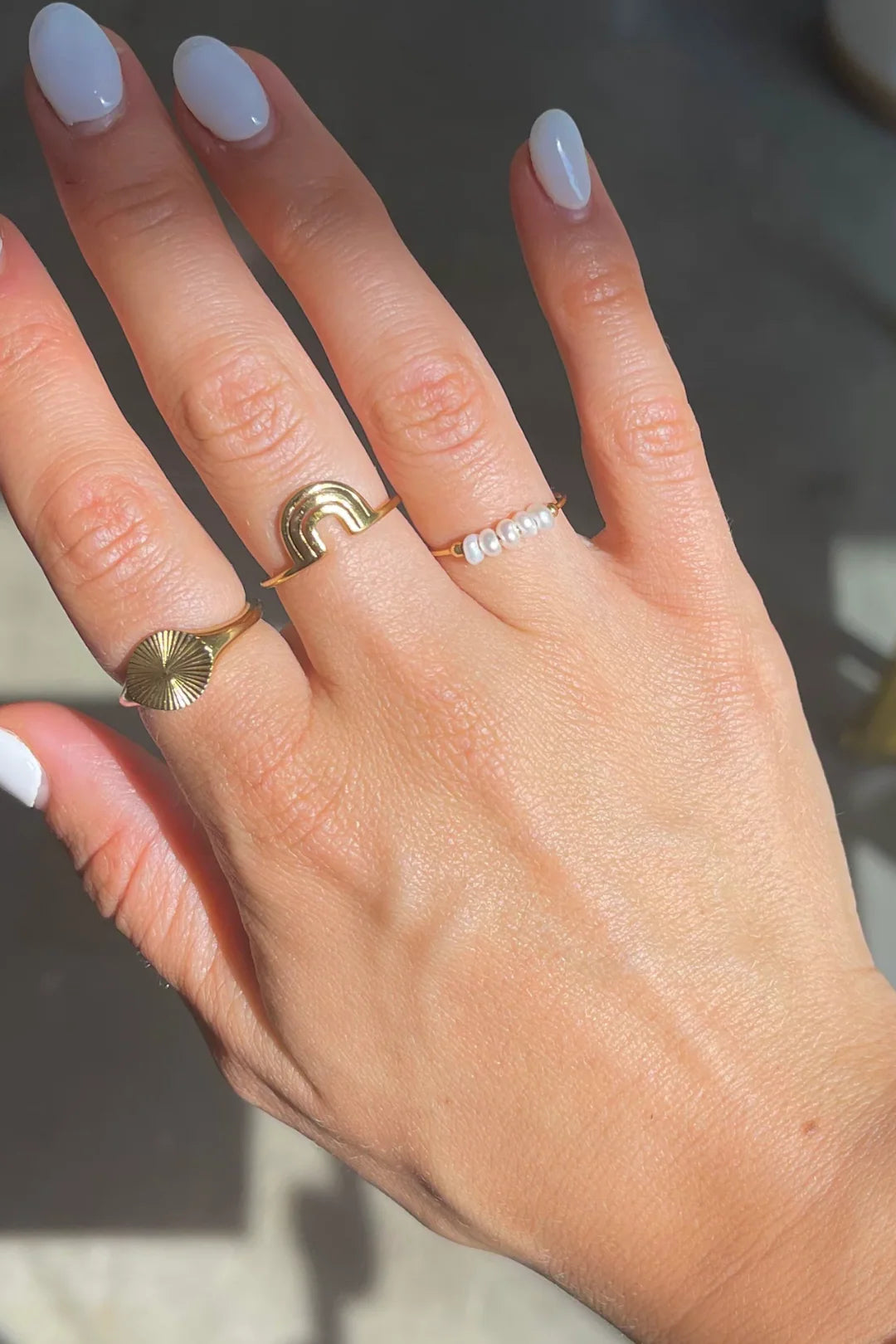 Hand wearing multiple gold rings including Polly pearl ring with a white nails 