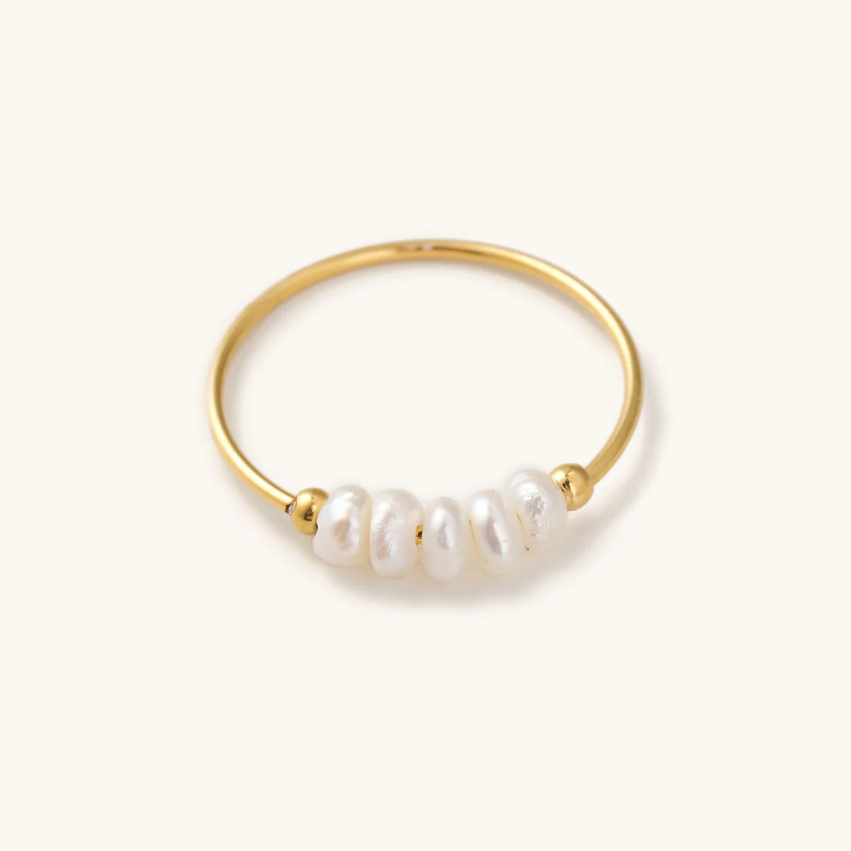 Simple, thin, Gold ring with multiple pearls laying on a white background