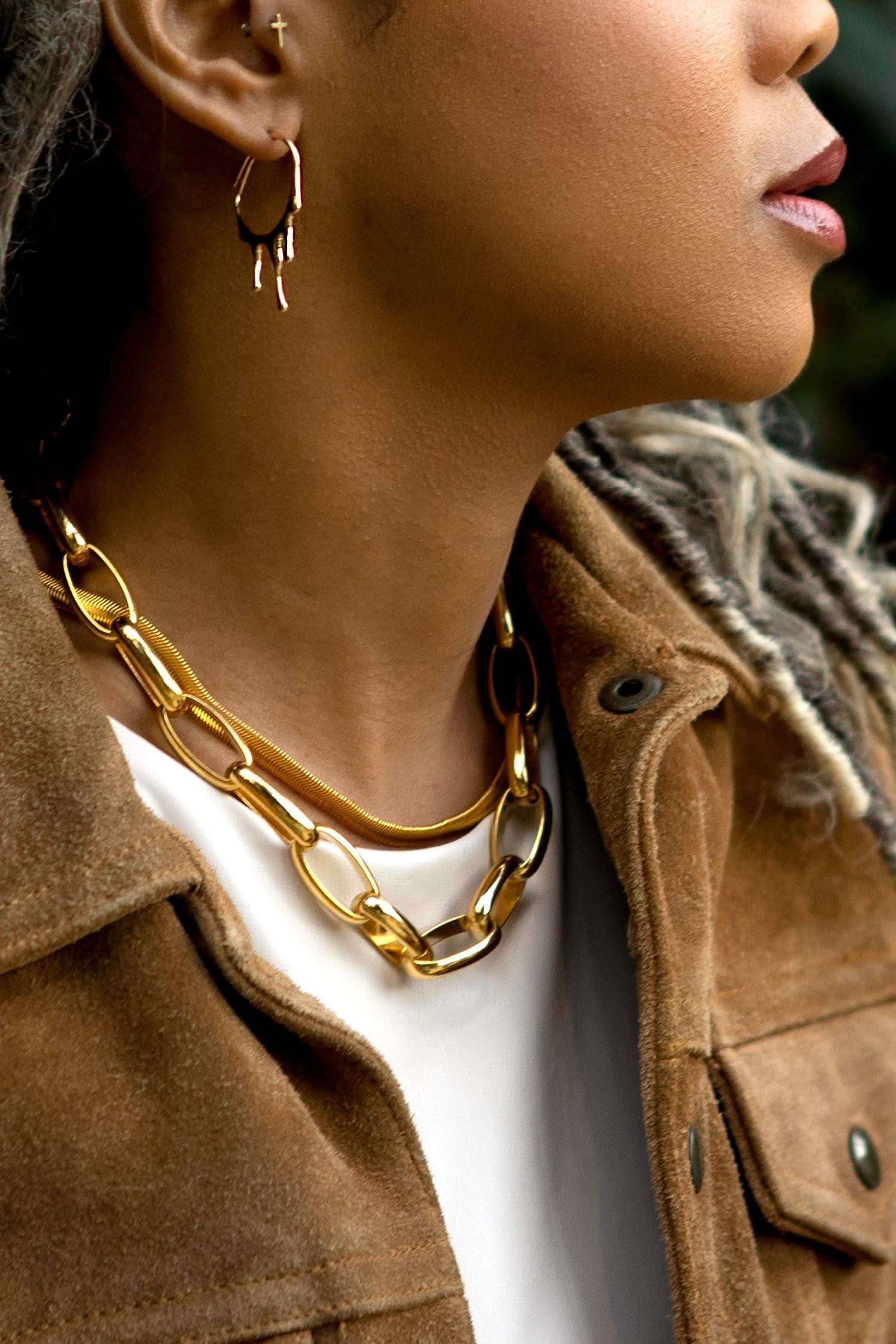 Close-up of a person wearing gold chain necklaces and earrings.
