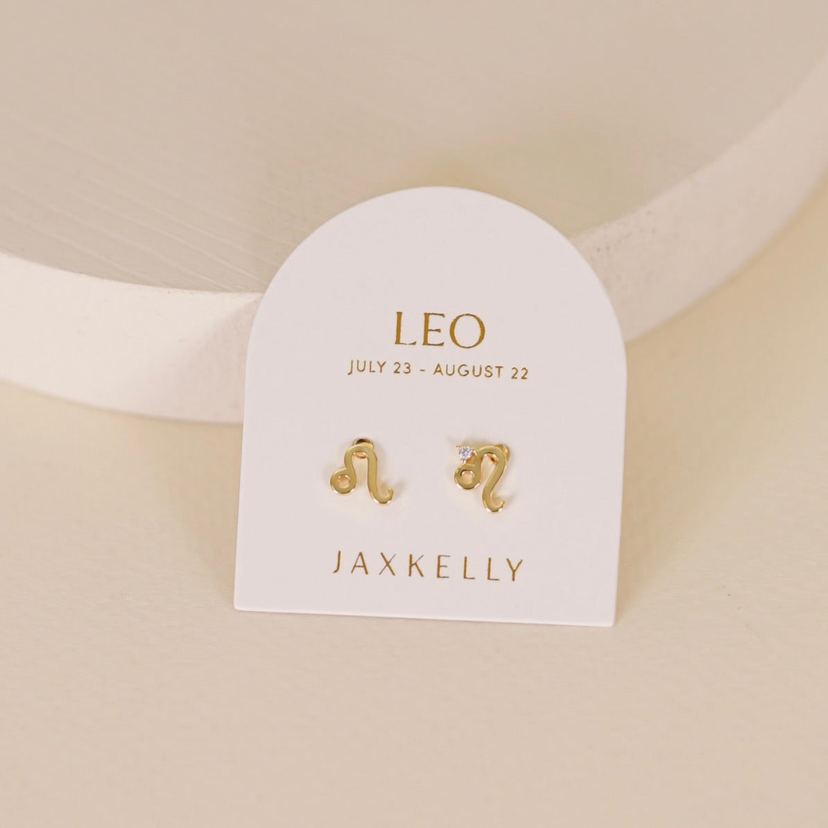 Gold zodiac charm studs in the shape of Leo astrological sign displayed on earring card