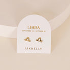 Gold zodiac charm studs in the shape of libra astrological sign displayed on earring card