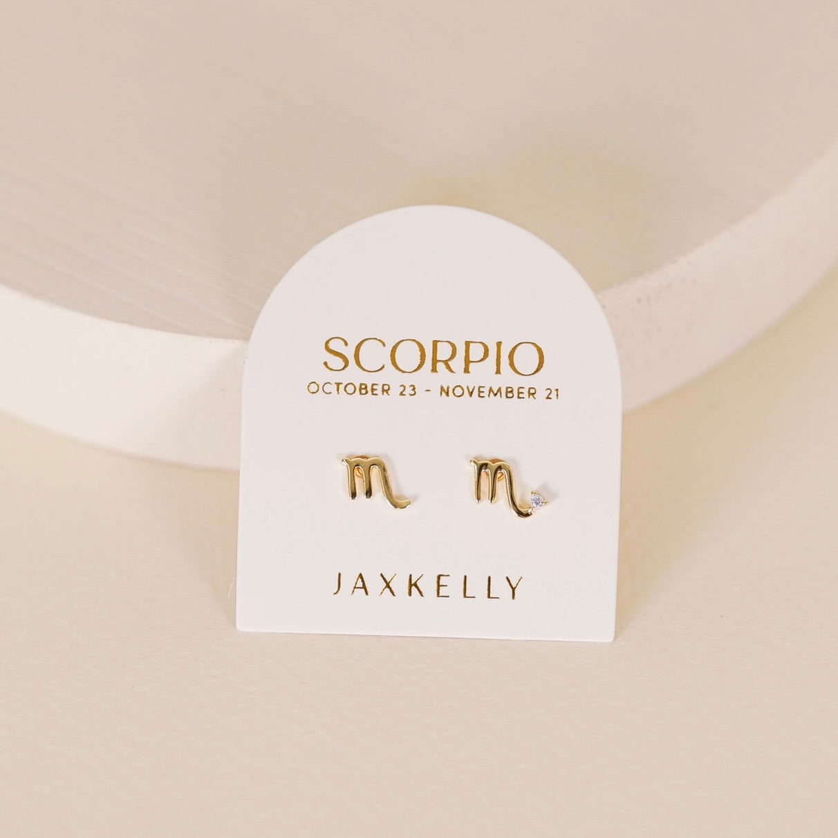 Gold zodiac charm studs in the shape of Scorpio astrological sign displayed on earring card 