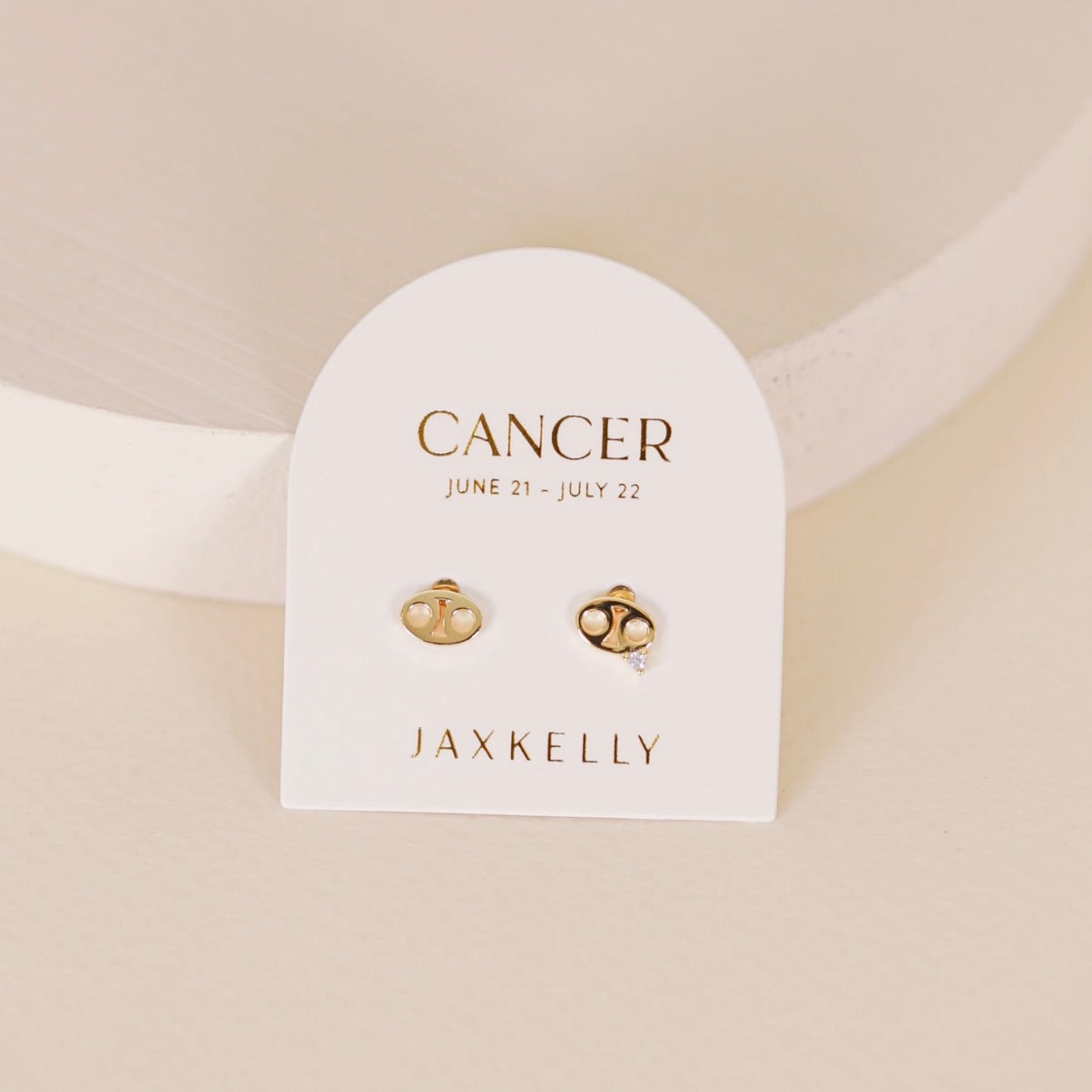 Gold zodiac charm studs in the shape of cancer astrological sign displayed on earring card