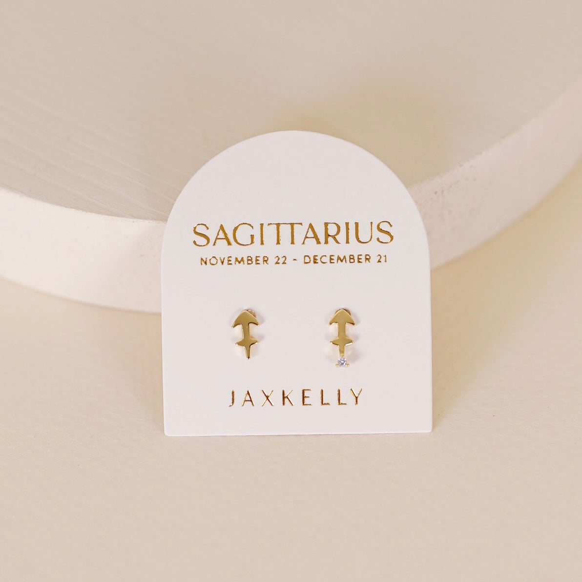 Gold zodiac charm studs in the shape of Sagittarius astrological sign displayed on earring card