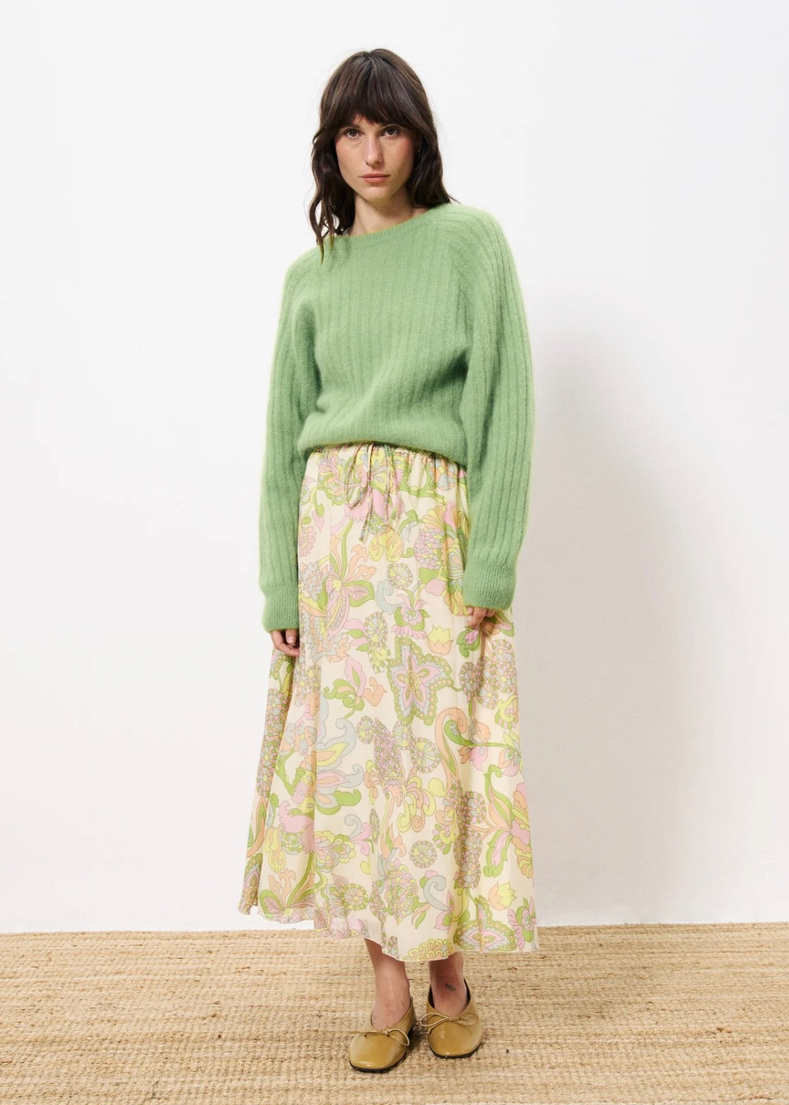 Woman wearing green sweater with pastel floral long skirt and ballet flats