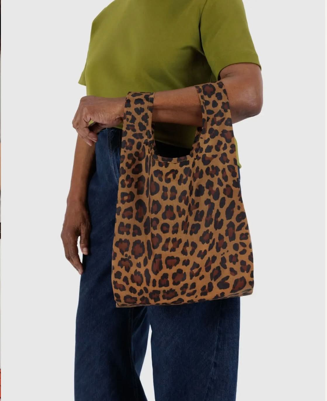 Woman carrying BAGGU leopard print reusable bag while wearing green top and jeans