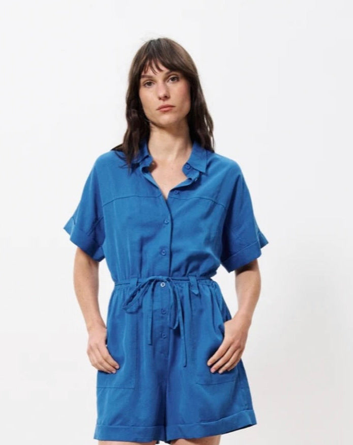 Woman wearing blue short sleeve button romper with front tie and leopard flats 