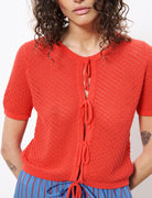 Woman wearing red knit style sweater cardigan with three adjustable string ties in the front 