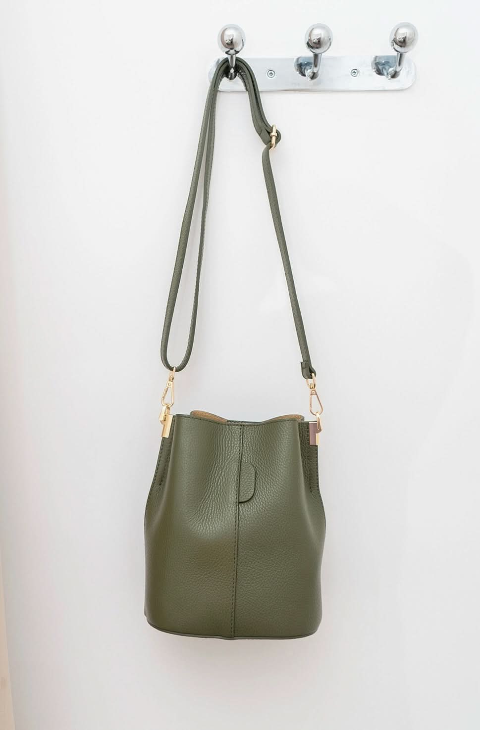 Green leather handbag with a strap hanging on a white wall.